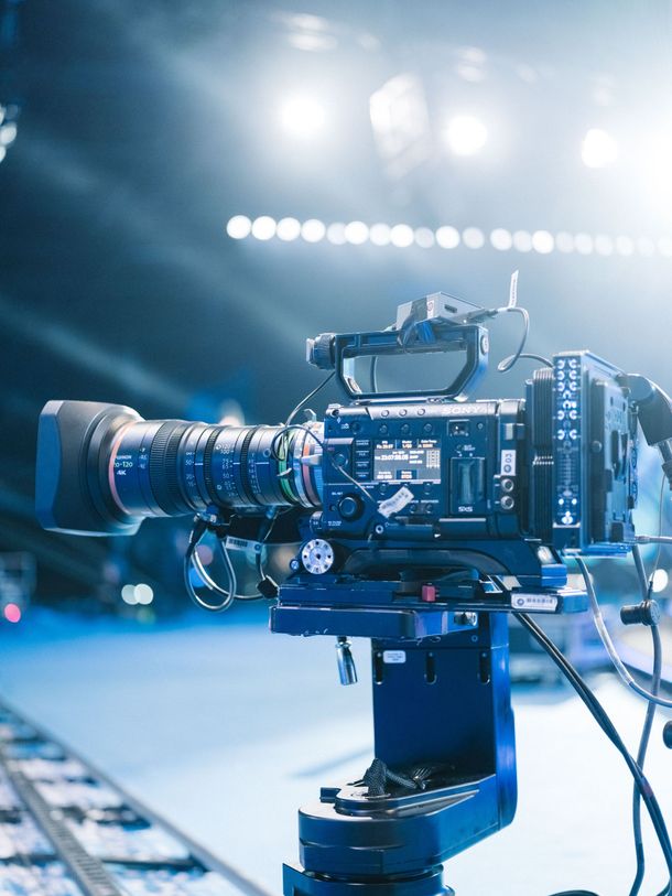 Professional video camera on a tripod in a blue-lit studio or stage setting