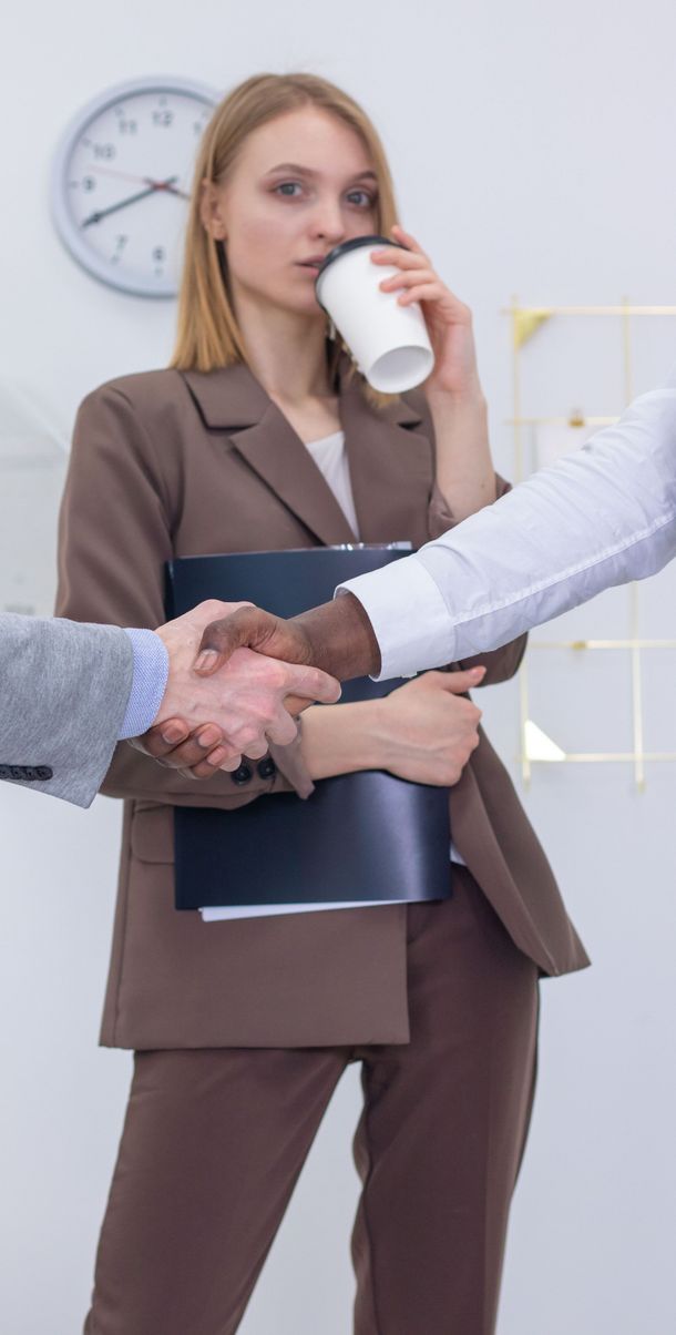 Businesswoman holding a coffee and notebook, shaking hands in an office setting