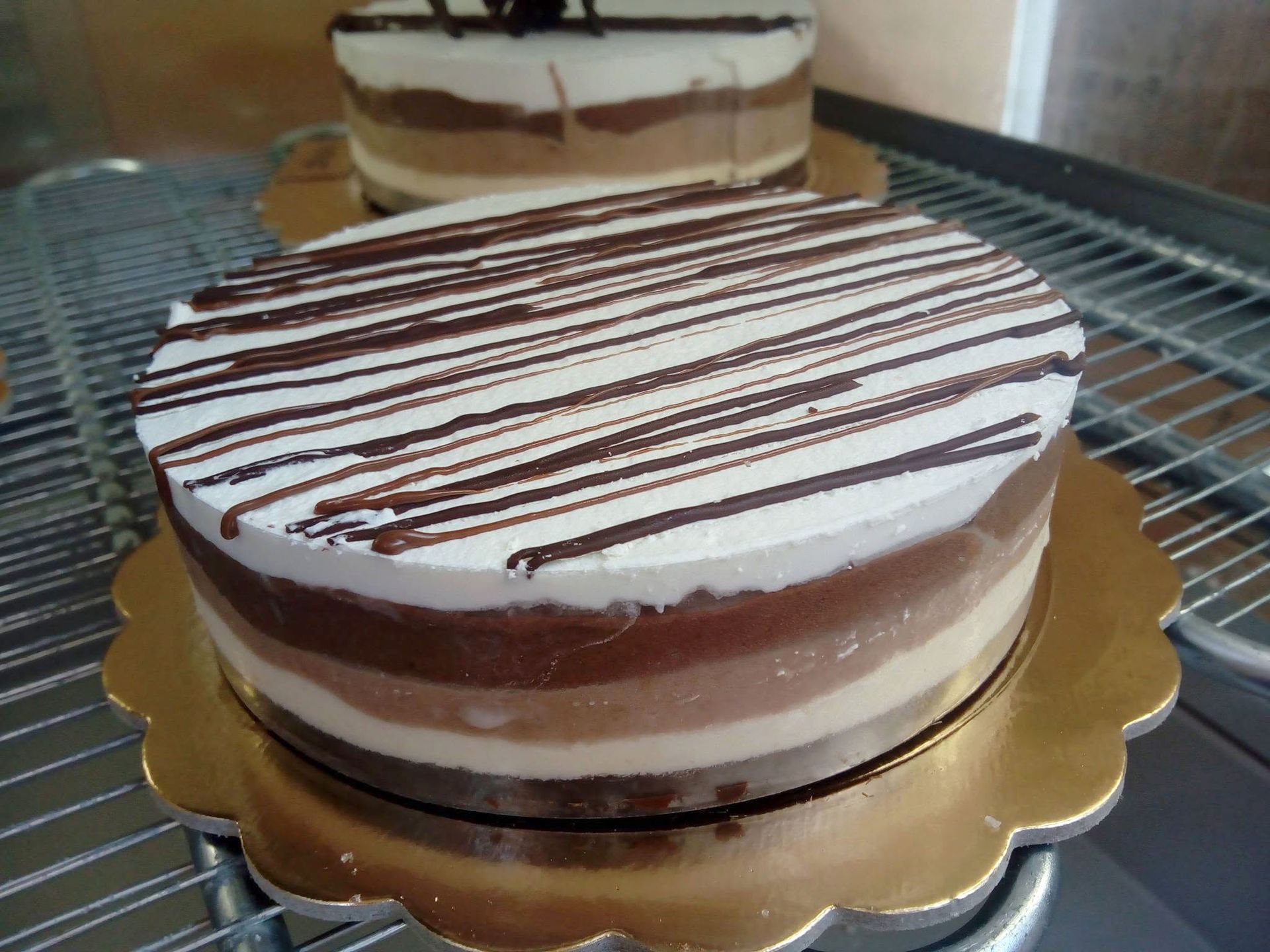 Torta rotonda a strati al cioccolato e panna con glassa bianca e decorazione al cioccolato, servita su un vassoio dorato.