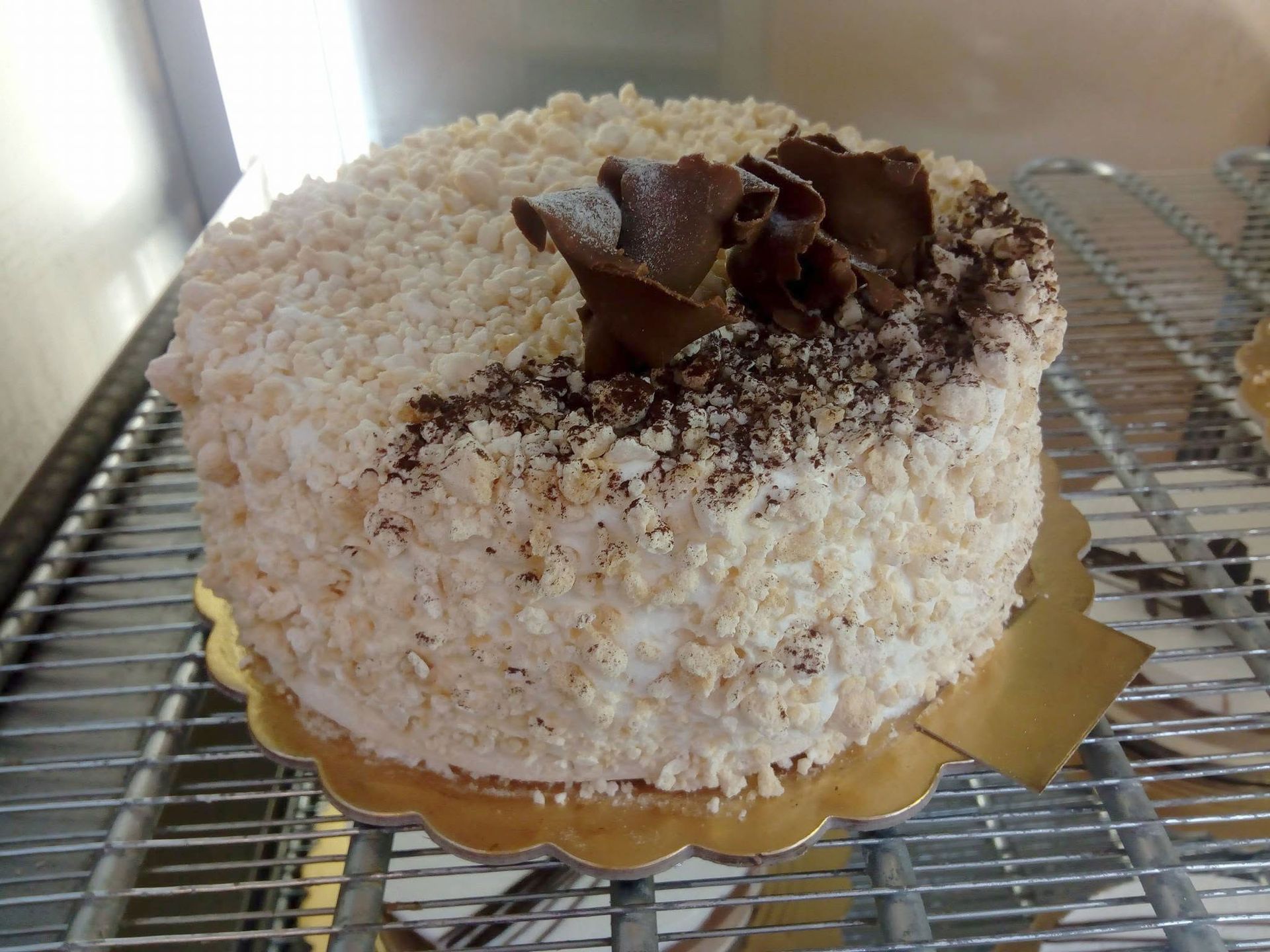 Torta rotonda al cocco decorata con riccioli di cioccolato, su un vassoio dorato appoggiato su una griglia metallica.