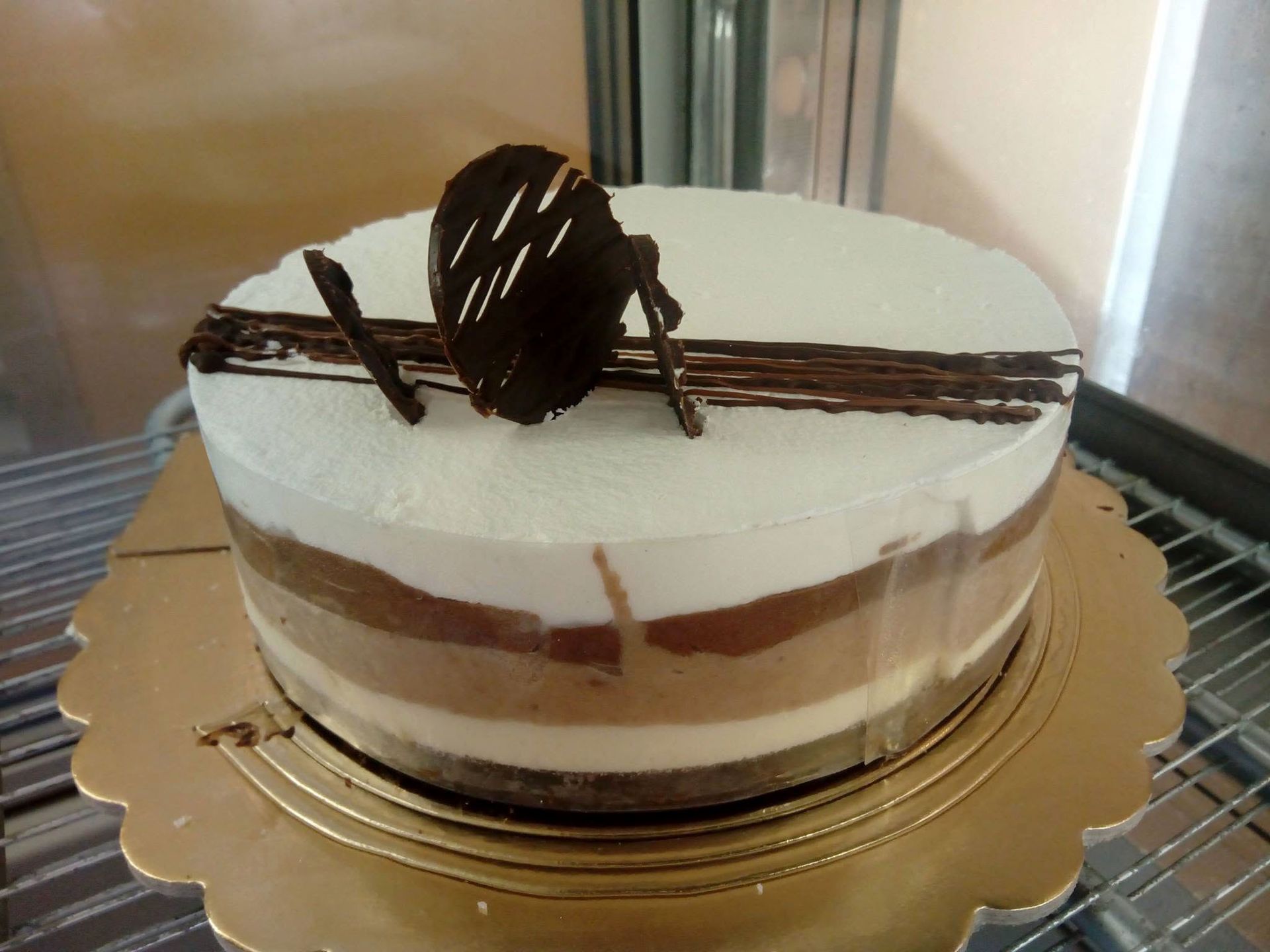 Torta a strati al cioccolato e bianca con decorazione a strisce di cioccolato su un vassoio dorato.