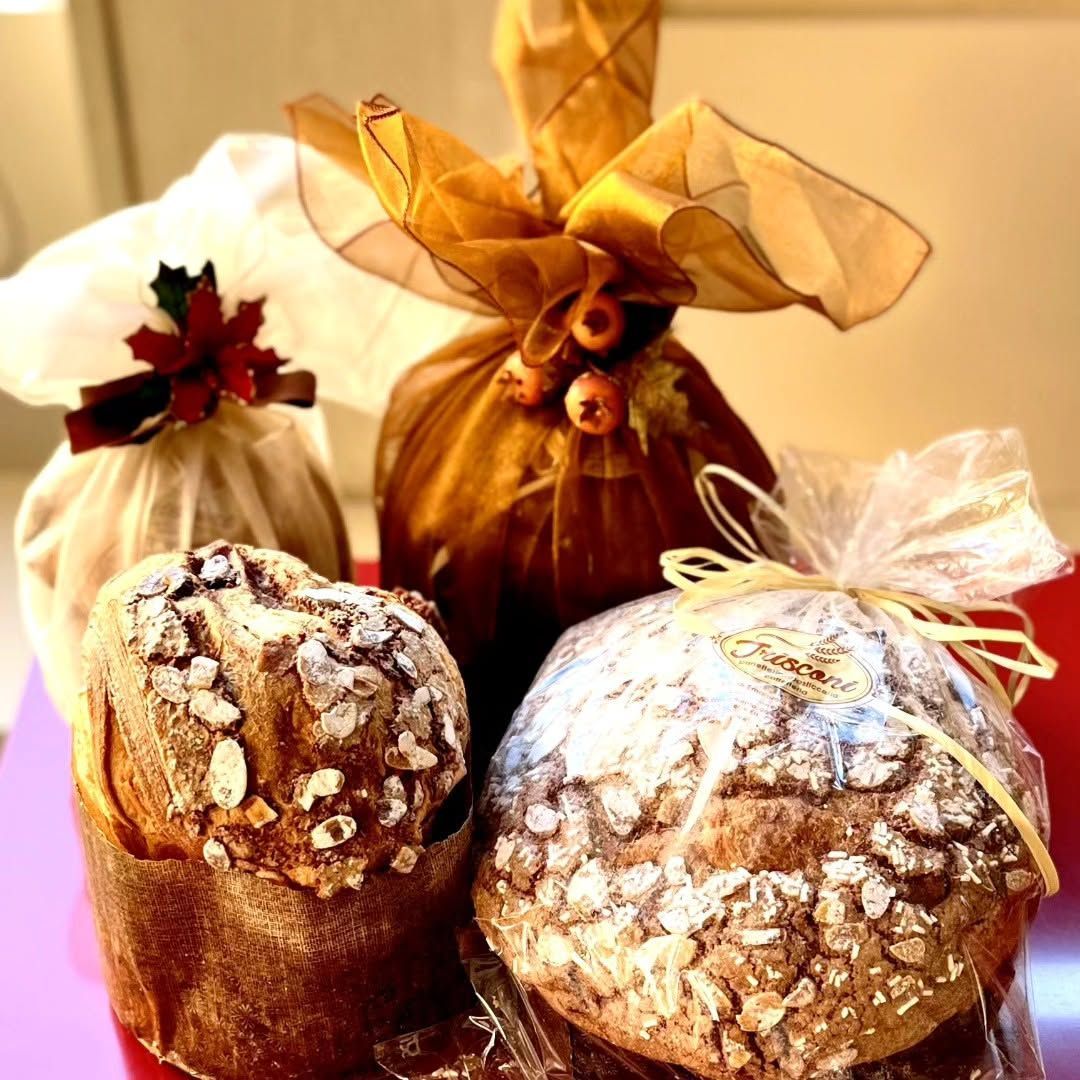 Assortimento di pagnotte festive avvolte in carta e nastri, tra cui dolcetti tipo panettone ricoperti di zucchero a velo.