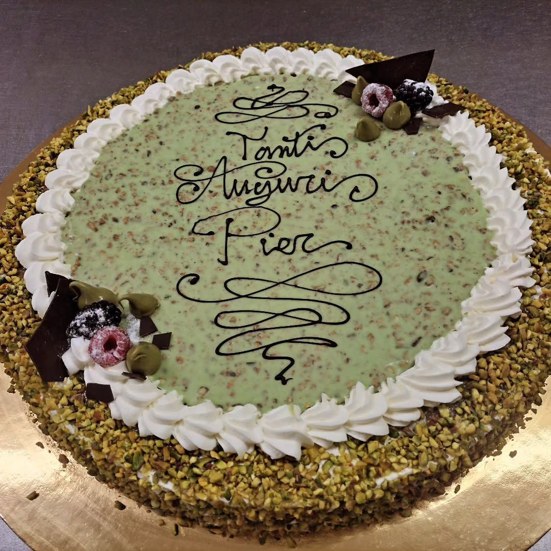 Torta rotonda al pistacchio con glassa bianca, decorata con fiori di sac à poche e scritta a mano 