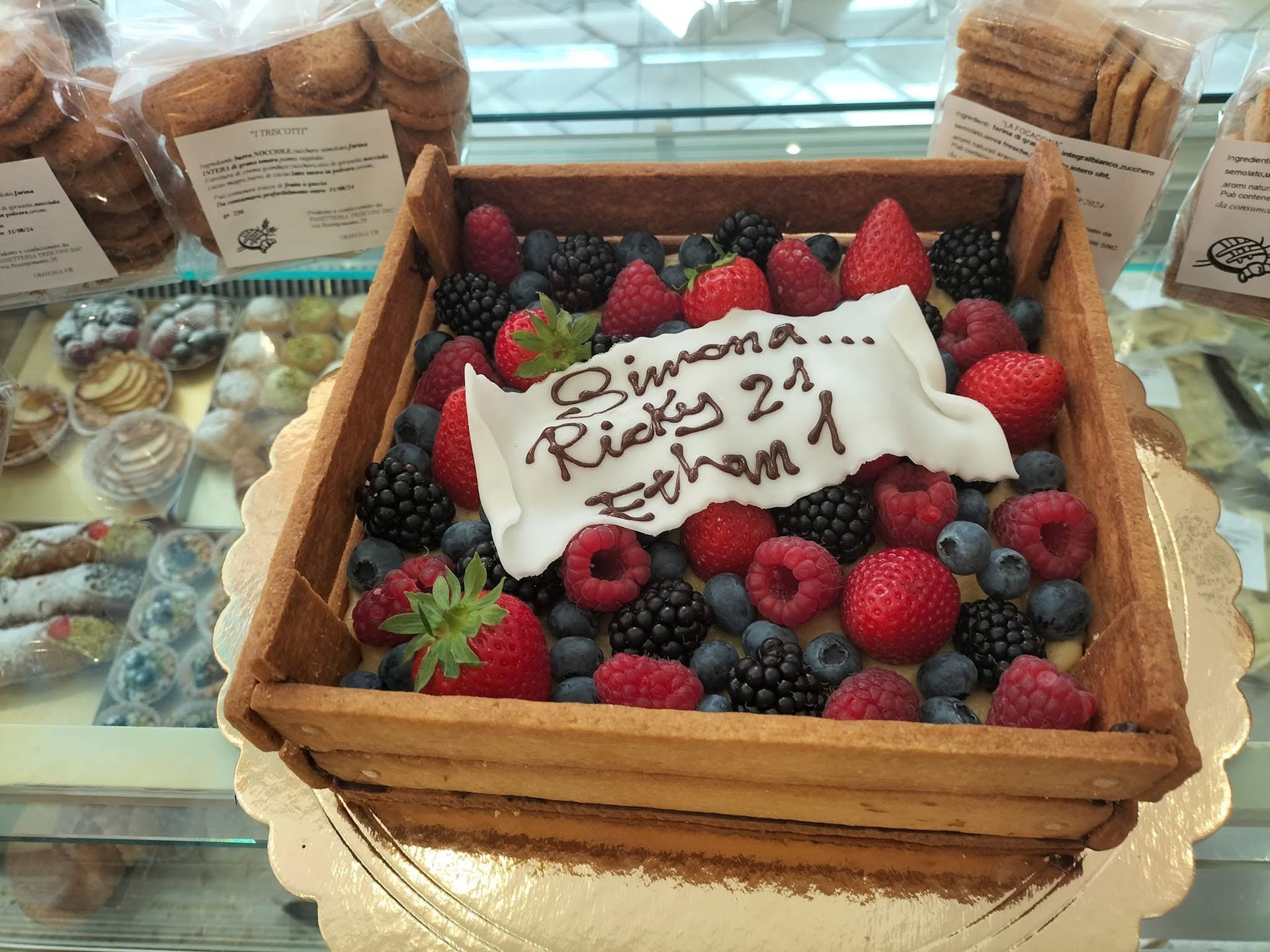 Torta decorata con frutti di bosco in un cestino di vimini con un messaggio di auguri scritto su glassa bianca.