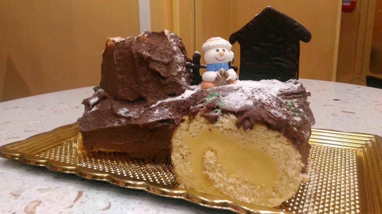 Tronchetto di cioccolato con ripieno di crema, sormontato da una piccola statuina di pupazzo di neve su un tavolo.