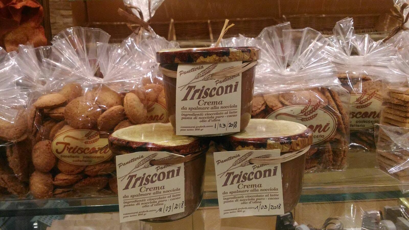 Vetrina espositiva con prodotti da forno Triscotti confezionati in sacchetti trasparenti e scatole rotonde, impilati su scaffali.