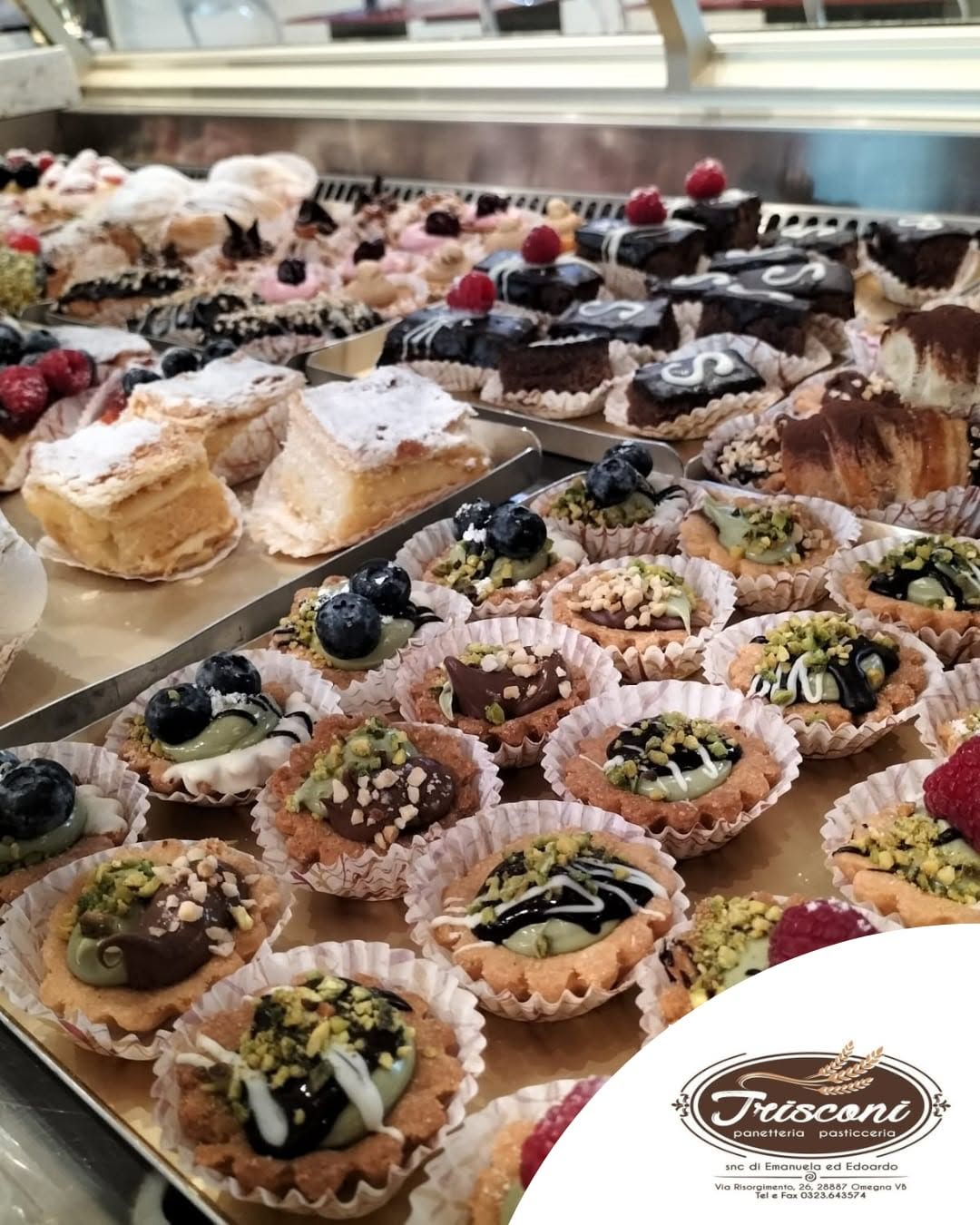 Vassoio di pasticcini e crostatine assortite con frutti di bosco e zucchero a velo in una vetrina da pasticceria.