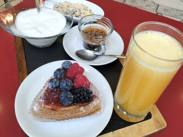 Una tavola apparecchiata per la colazione con crêpe ai frutti di bosco, yogurt, cereali e succo d'arancia.