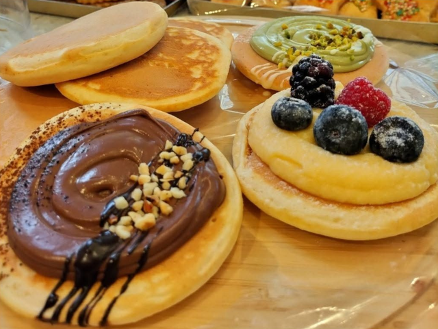 Pancake assortiti con cioccolato, frutta e panna, serviti su un vassoio di legno.