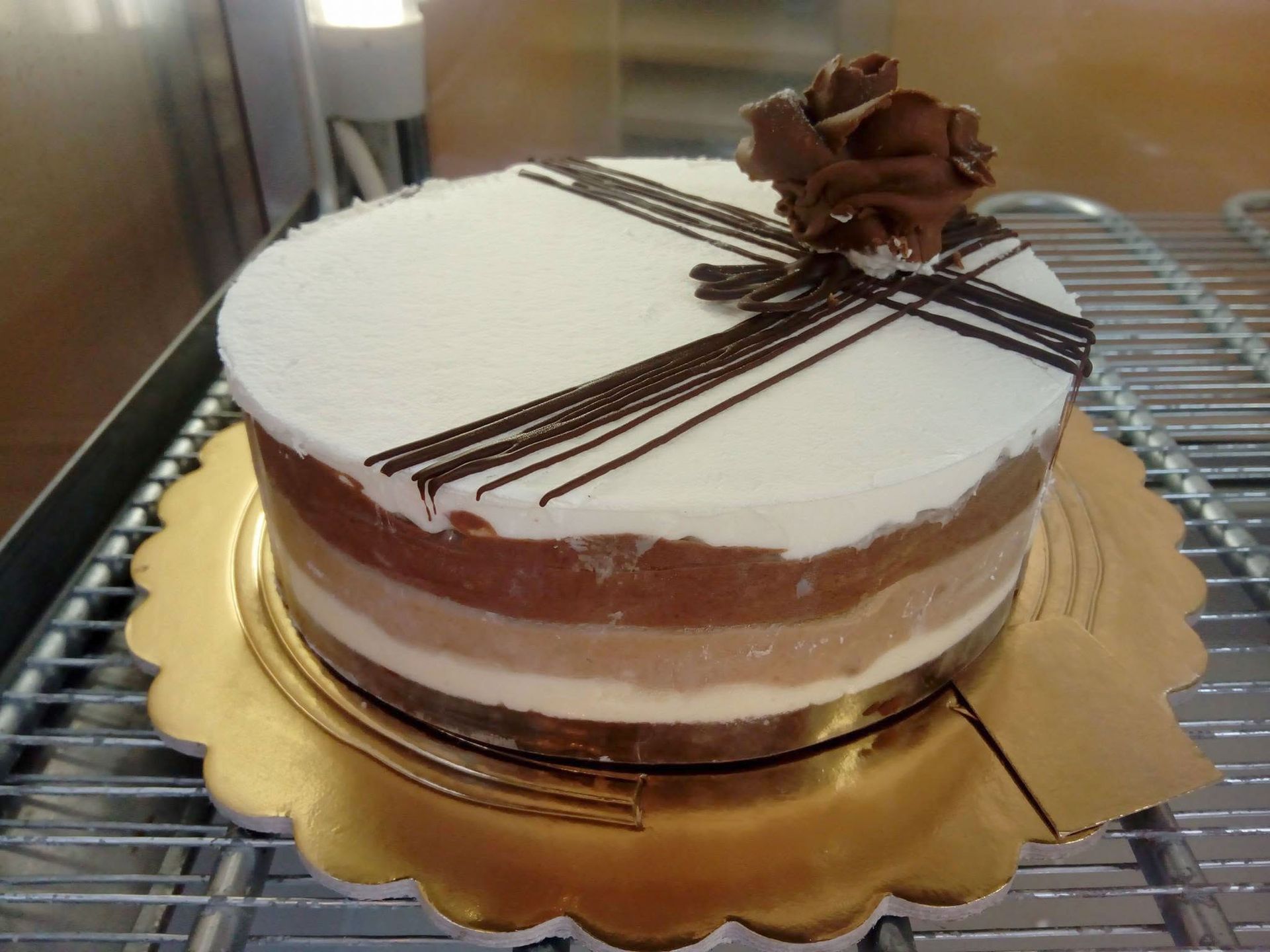 Torta rotonda al cioccolato con glassa bianca e decorazione a nastro di cioccolato, servita su un vassoio dorato.