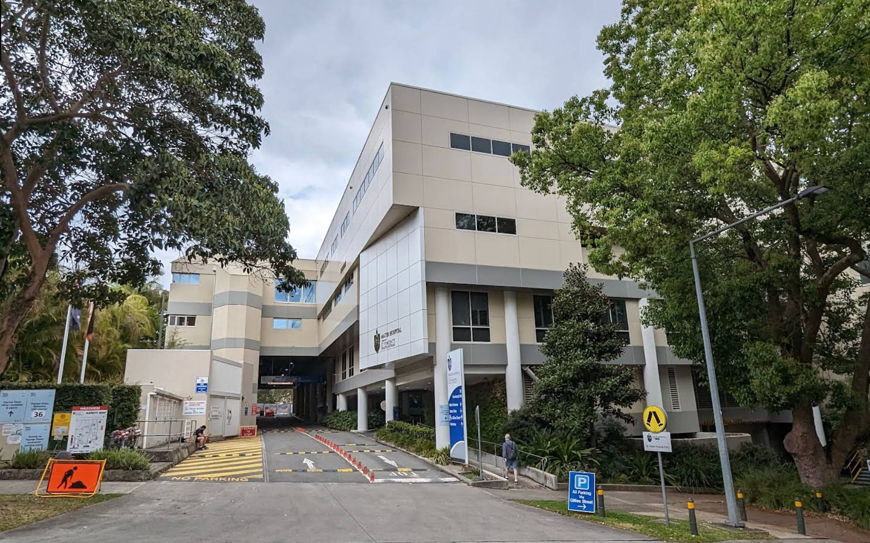 Exterior view of a multi-story, beige building with trees in front. Entrance has ramps and traffic control.