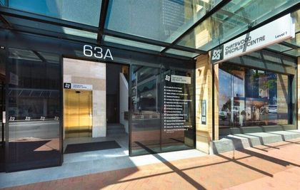 Entrance to building at 63A. Glass doors with signage, gold elevator doors, and sidewalk.