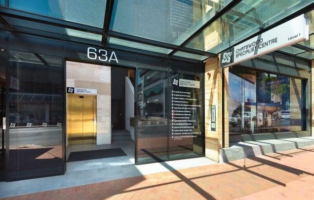 Entrance to building at 63A. Glass doors with signage, gold elevator doors, and sidewalk.