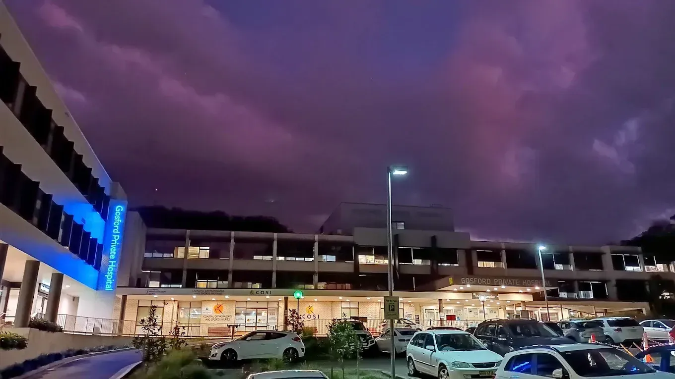 Hospital building exterior at night with stormy purple clouds and parked cars.