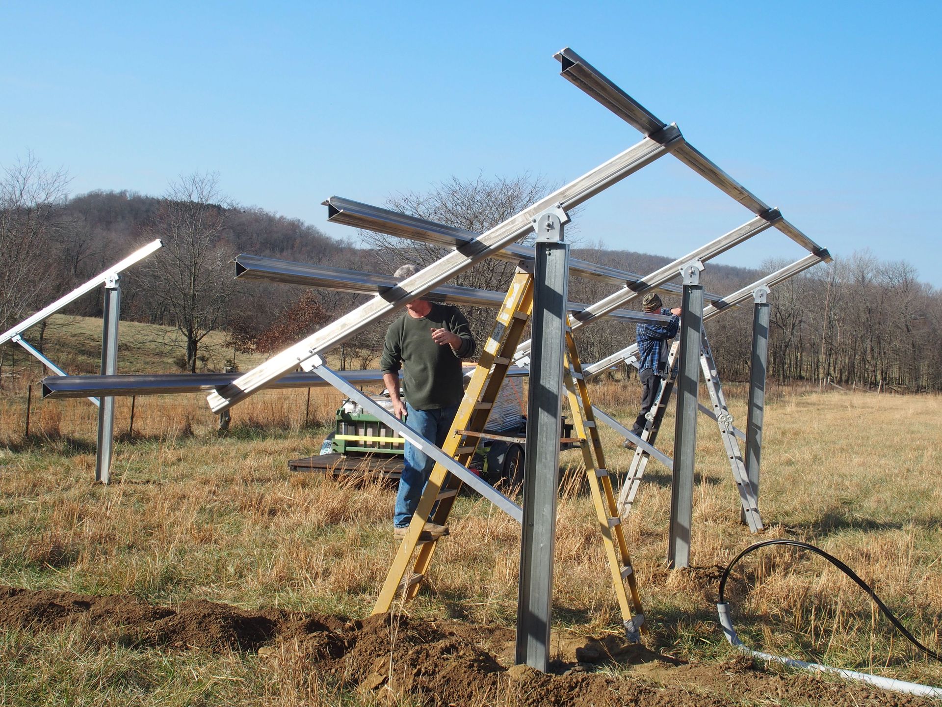 A man is standing on a ladder in front of a metal structure in a field