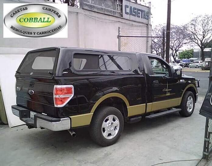 Una camioneta Ford negra con una cubierta para la caja a juego, también negra, estacionada en un lote pavimentado, con detalles inferiores en tono dorado.
