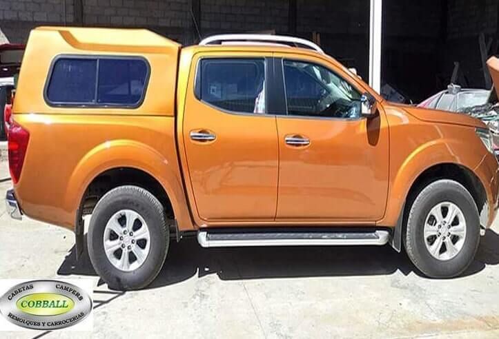 Una camioneta Nissan Navara naranja con una capota a juego, estacionada al aire libre, vista de lado.