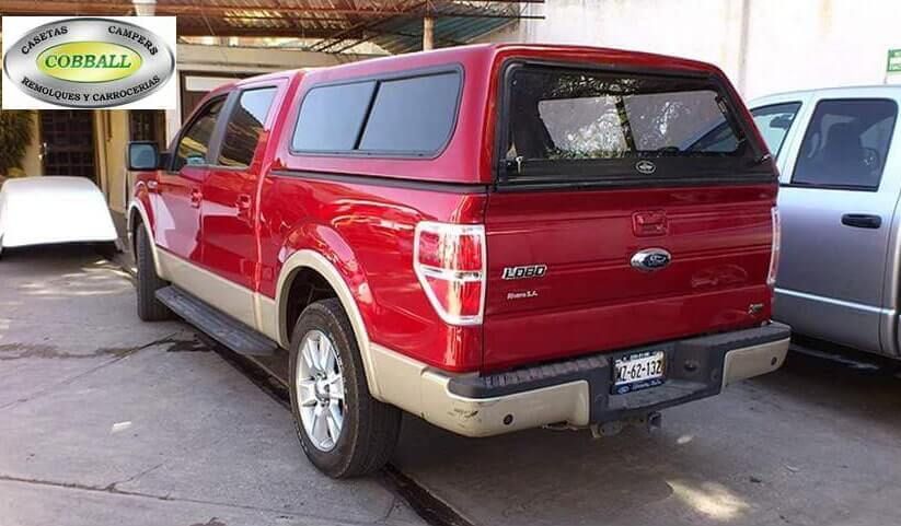 Una camioneta Ford roja con una capota a juego estacionada al aire libre, con un logotipo en una esquina.
