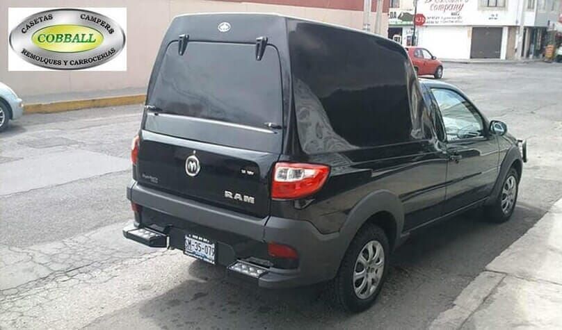 Una camioneta RAM negra con una caja de carga tipo camper estacionada en una calle pavimentada.
