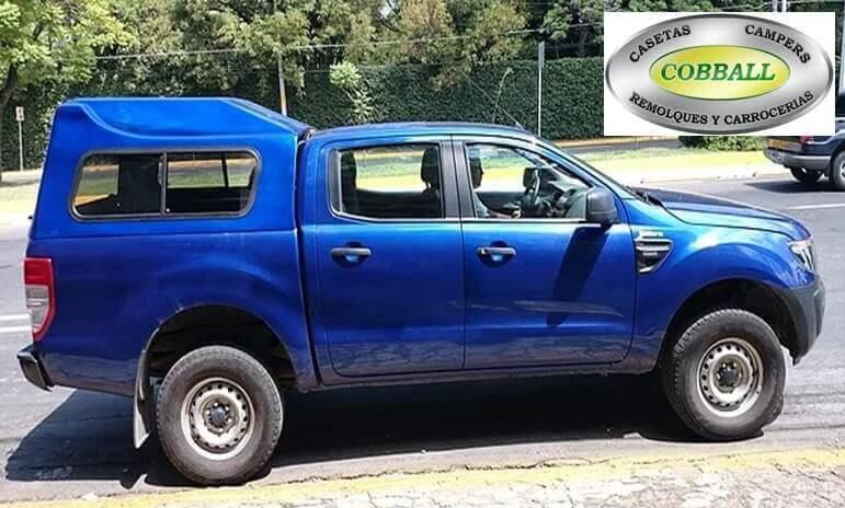 Camioneta Ford Ranger azul con una cubierta para la caja a juego, estacionada al aire libre con el logotipo de la marca Cobball en una esquina.