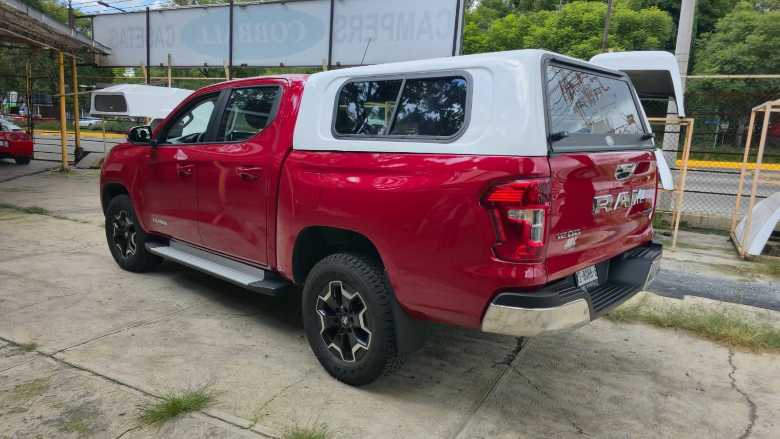 Una camioneta pickup roja de doble cabina con una caja de carga blanca estacionada en un lote pavimentado.