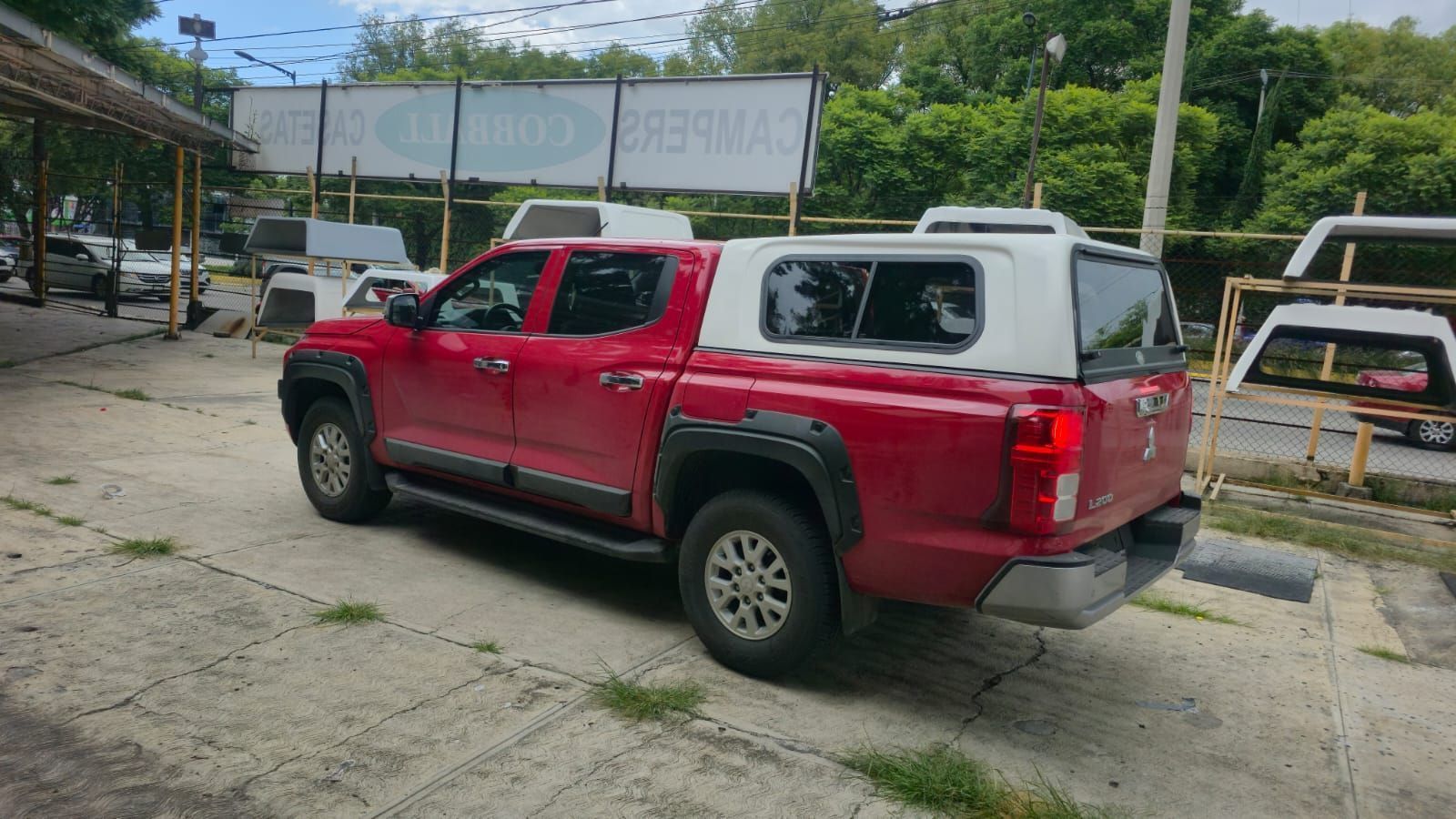 Una camioneta roja con una caja de carga blanca estacionada en un lote pavimentado de un concesionario.