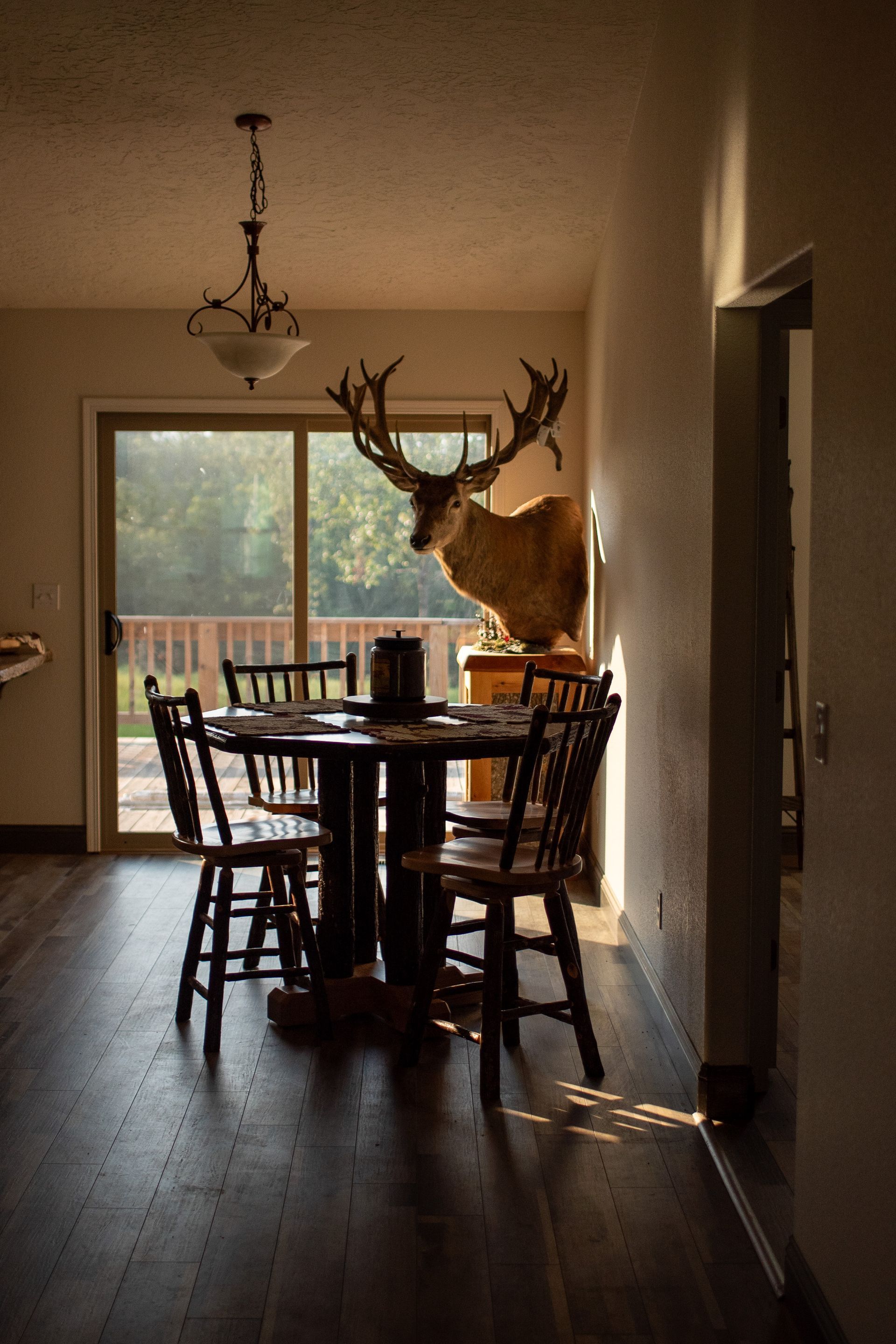A dining room with a table and chairs and a deer head on the wall