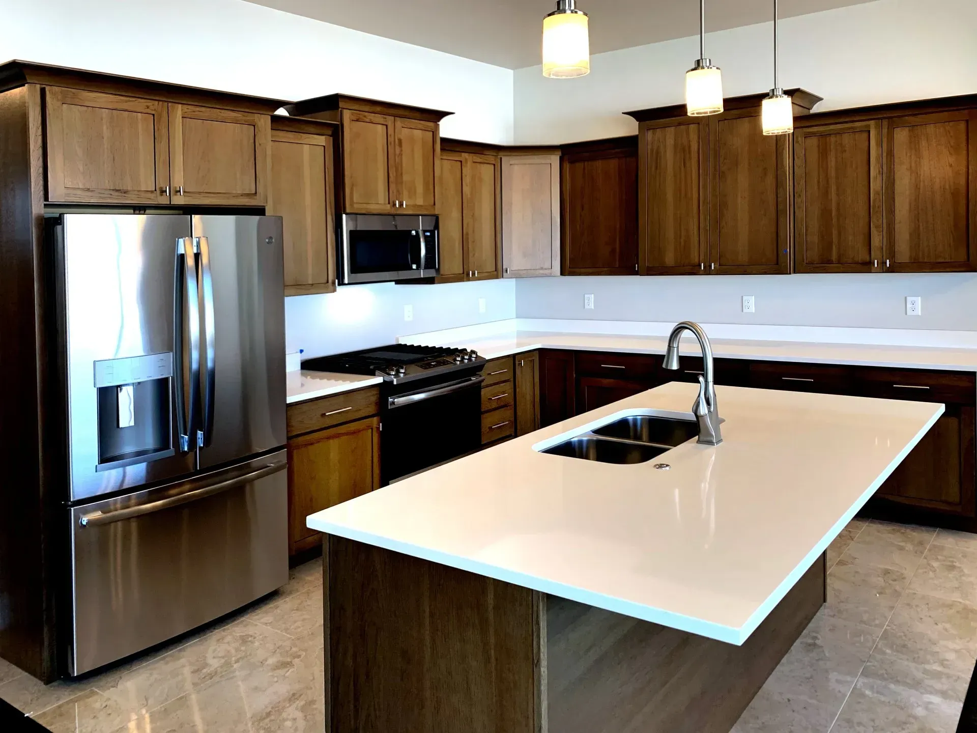 A modern kitchen featuring brown wooden cabinets, stainless steel appliances, a white quartz island, and tile flooring.