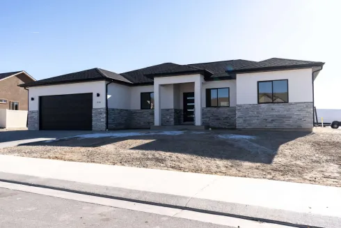A single-story modern house with a light stucco finish, stone veneer base, black roof, and an attached double garage.