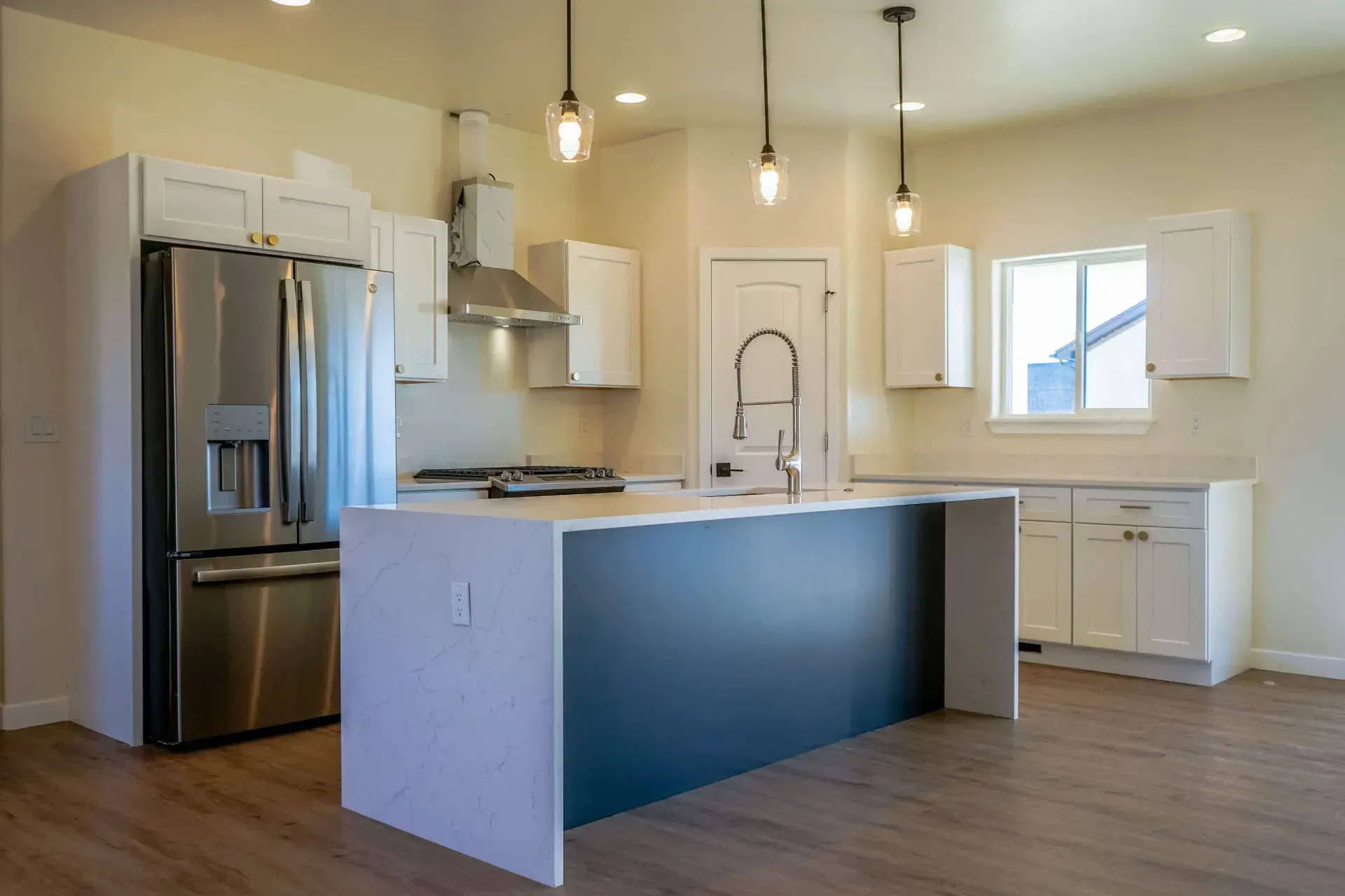 A modern kitchen with white cabinets, stainless steel appliances, a dark blue kitchen island, and wood-look flooring.