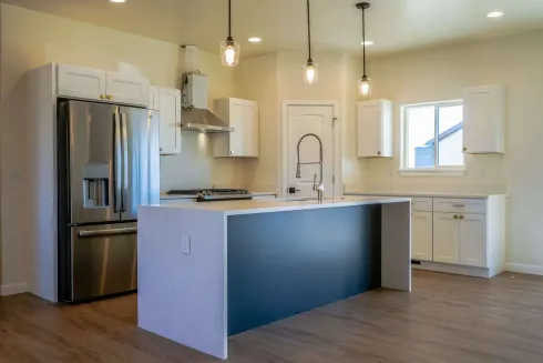 A modern kitchen with white cabinets, stainless steel appliances, a dark blue kitchen island, and wood-look flooring.