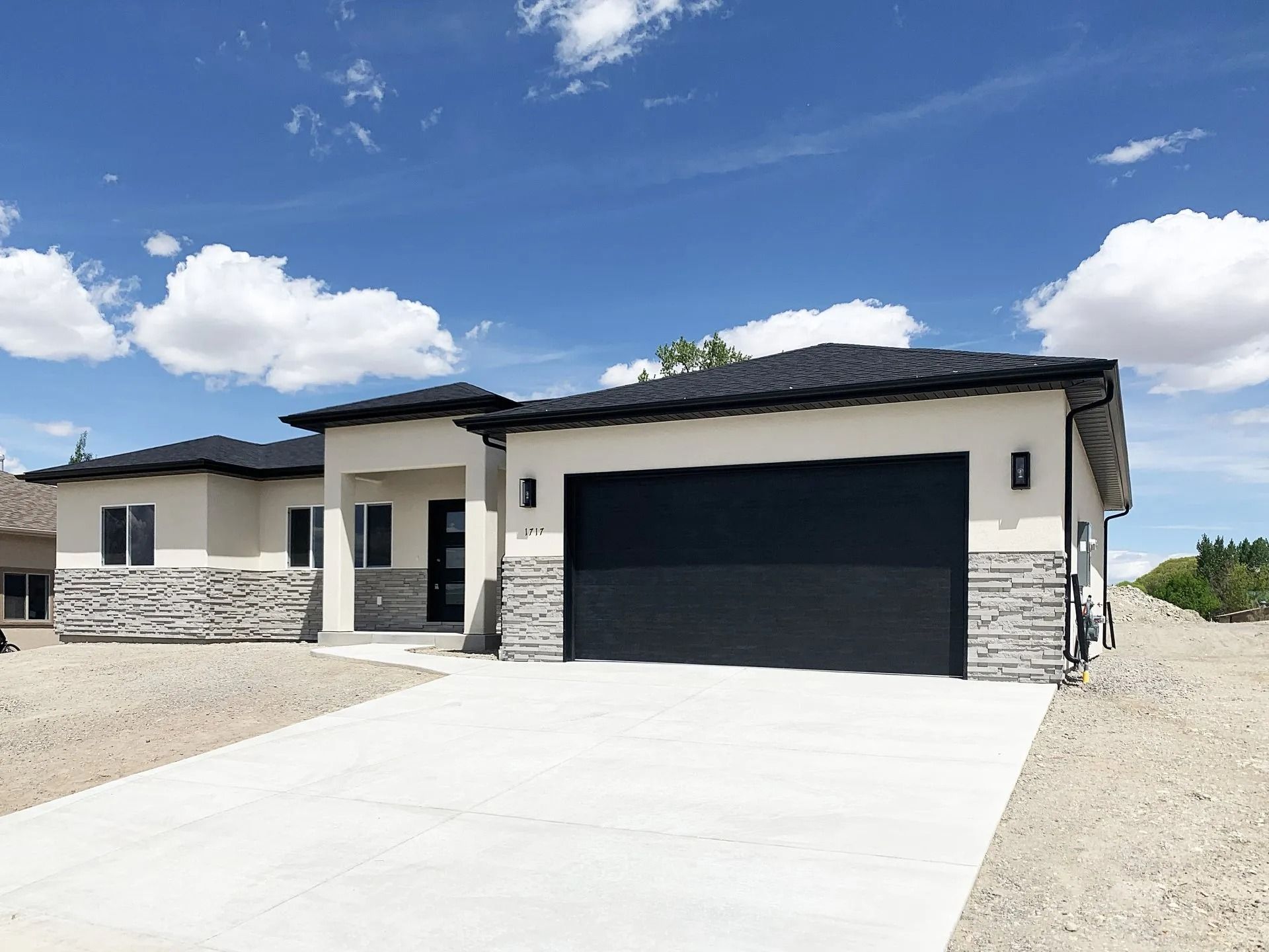 A modern single-story house with a cream stucco exterior, stone base, black roof, and a large black garage door.