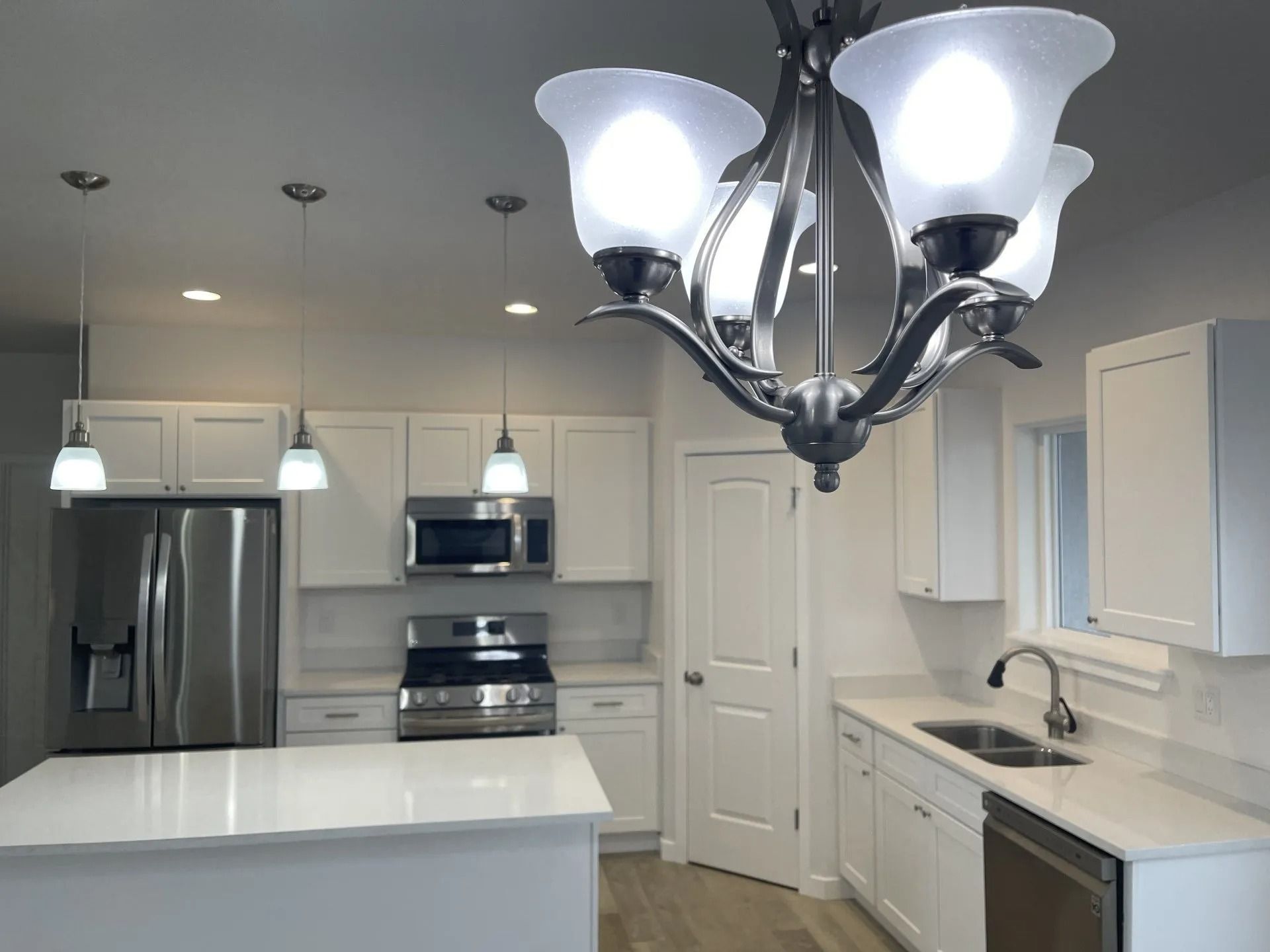 A modern kitchen featuring white cabinets, stainless steel appliances, white countertops, and a central chandelier.