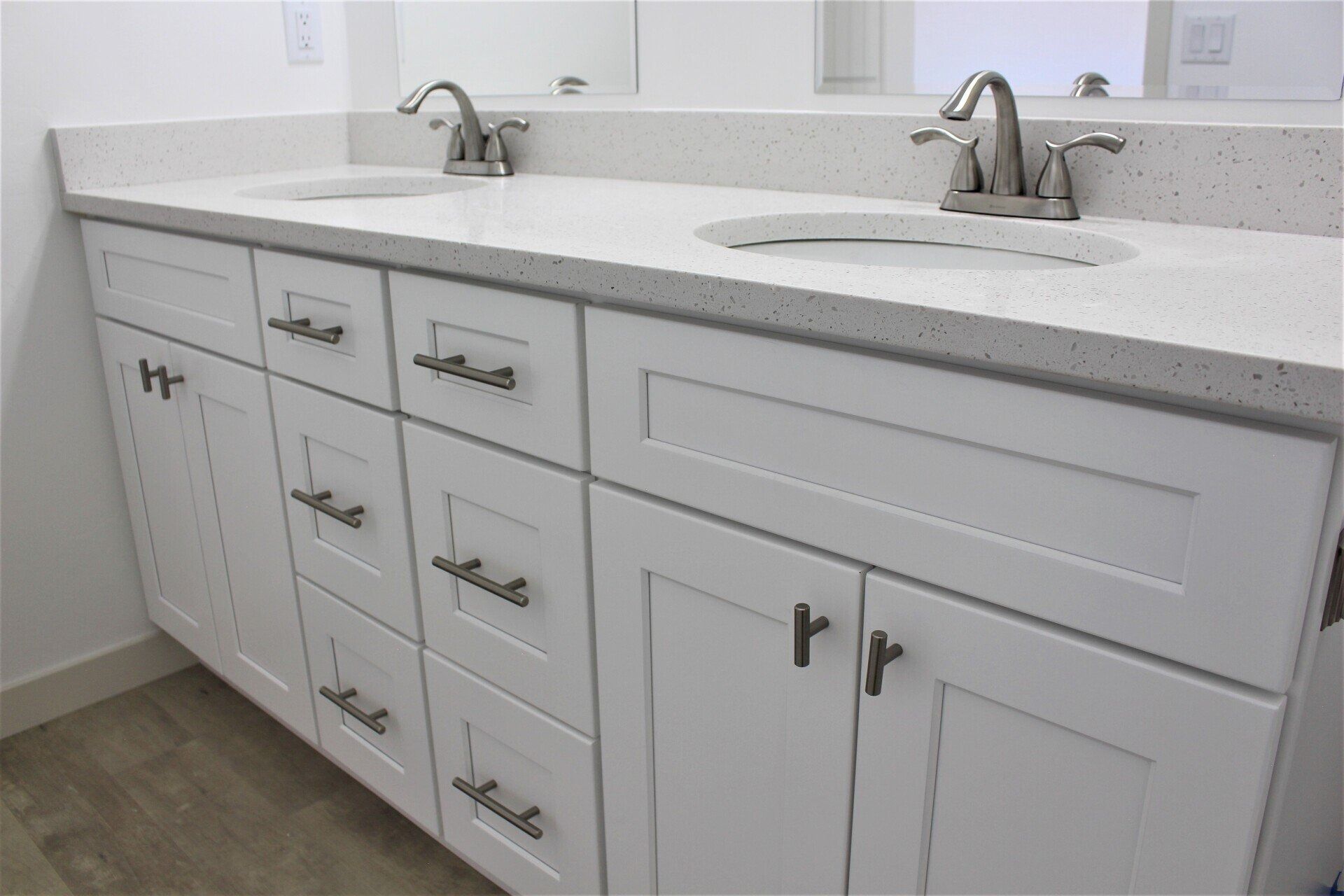 A white double-sink bathroom vanity with light quartz countertops, silver faucets, and shaker-style cabinets and drawers.