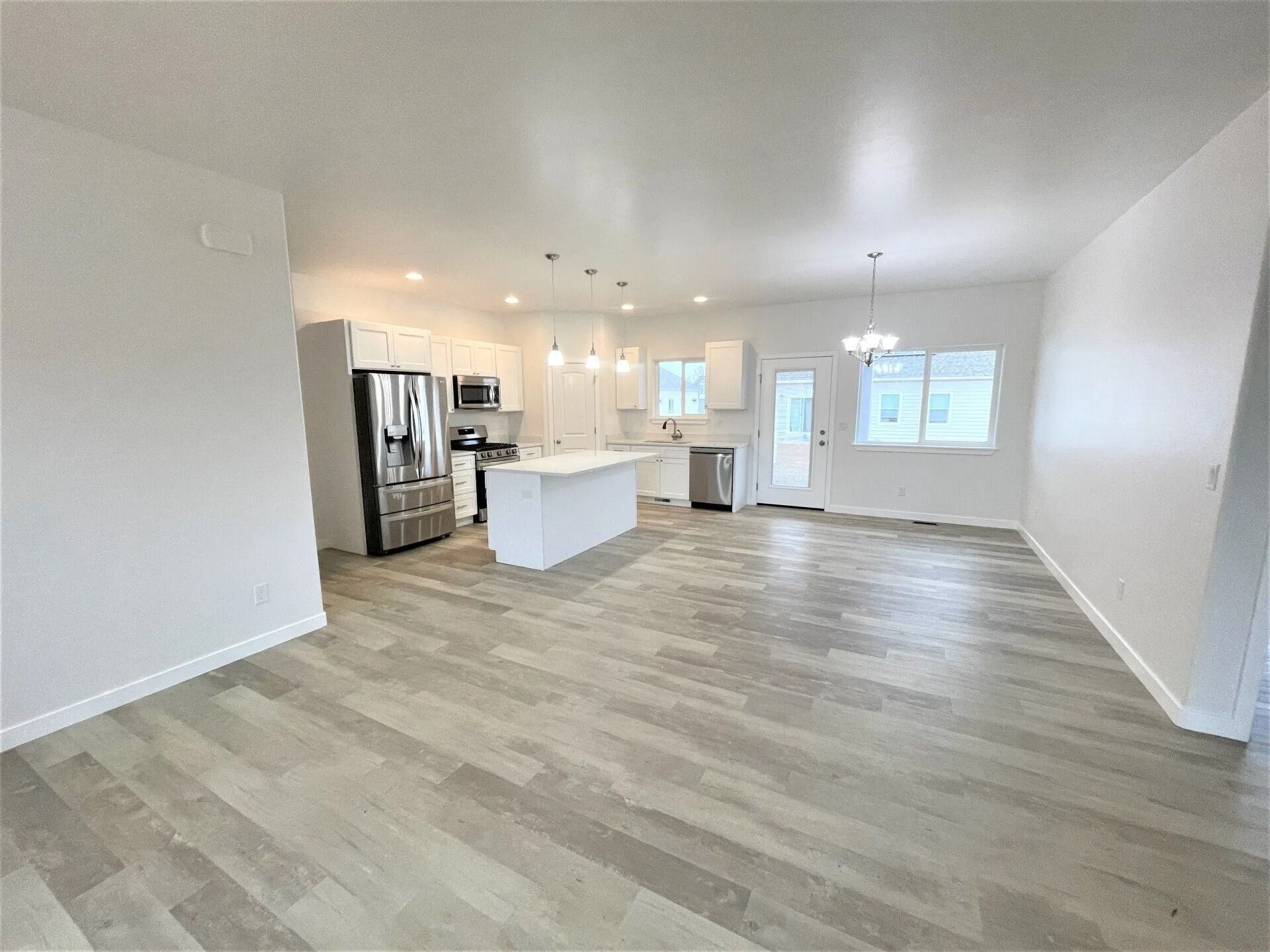 A modern open-concept home interior featuring a white kitchen, light grey wood-look flooring, and a dining area.