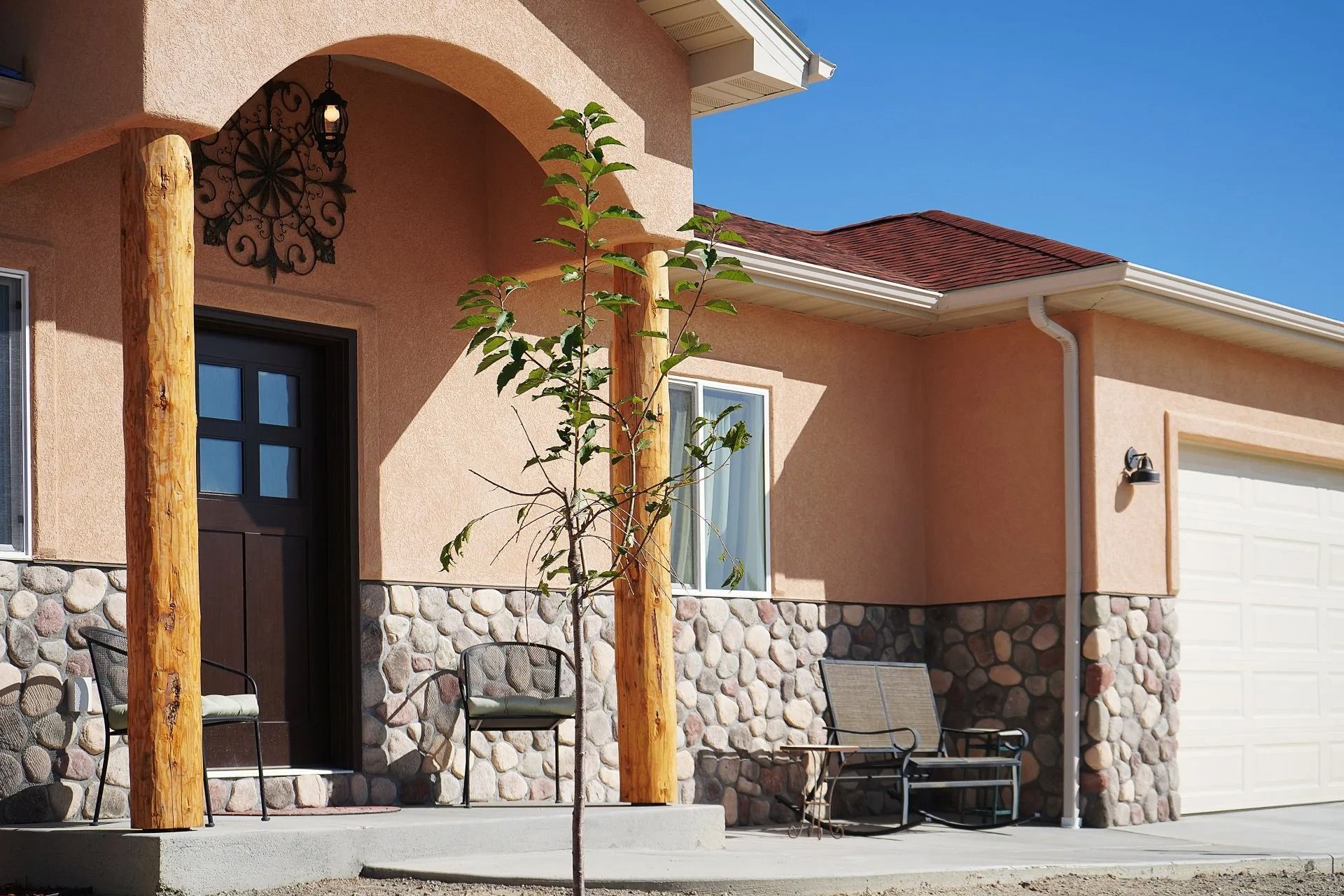 A peach-colored house exterior with stone wainscoting, an arched porch entry with wood pillars, and a white garage door.