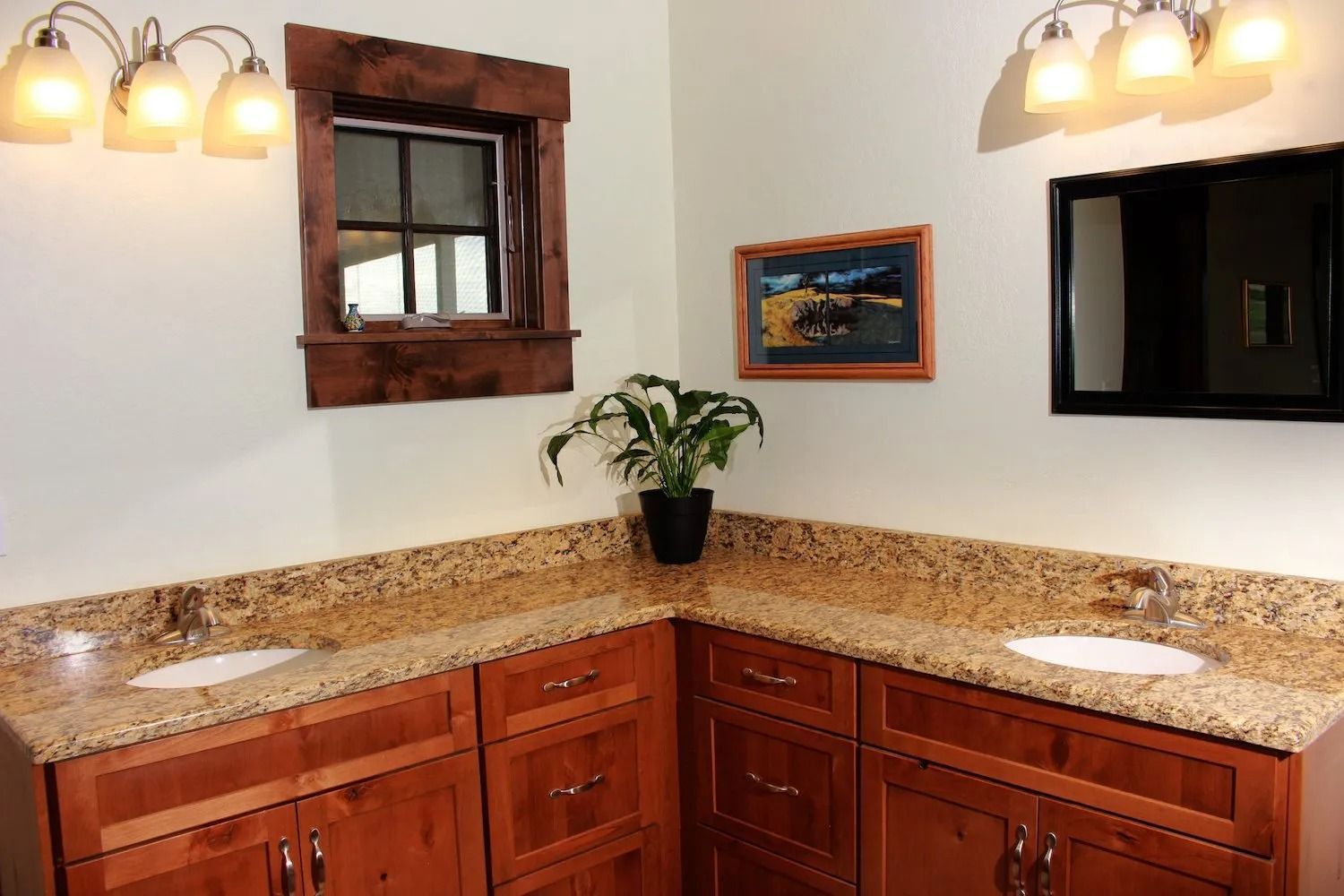 Double-sink bathroom vanity with wood cabinets, granite countertops, and two wall-mounted light fixtures.