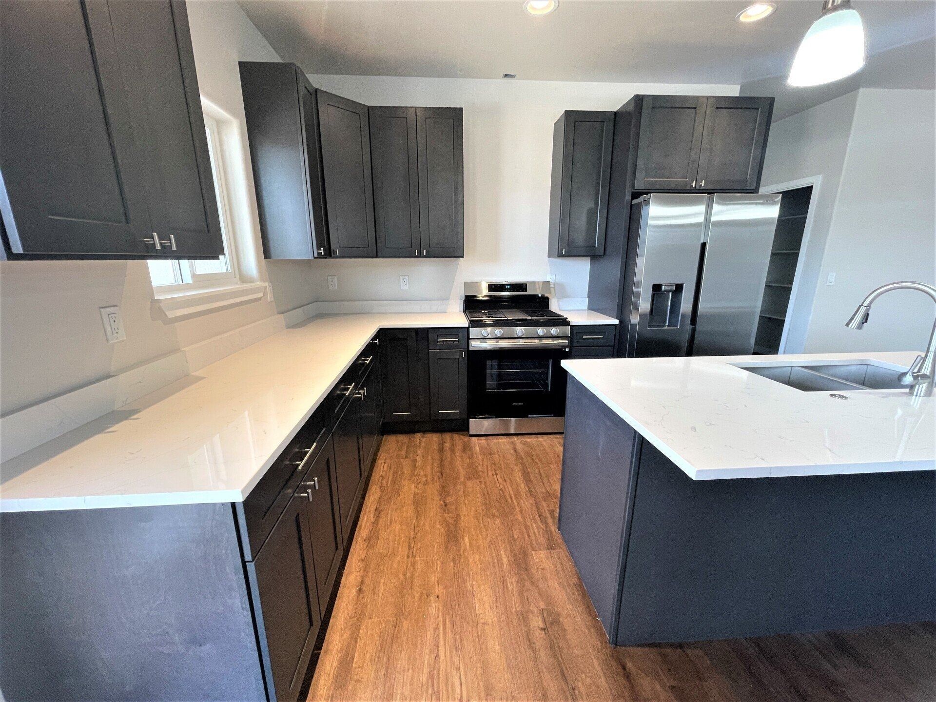 Modern kitchen with dark charcoal cabinetry, white quartz countertops, stainless steel appliances, and wood-tone flooring.