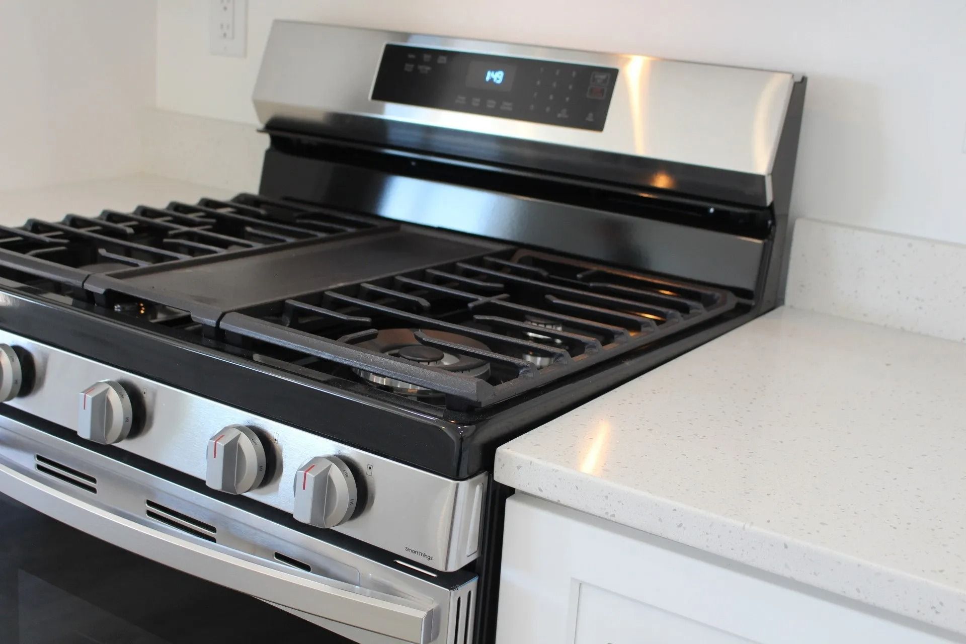 A stainless steel gas stove with a black cooktop and four control knobs, positioned against a white kitchen countertop.