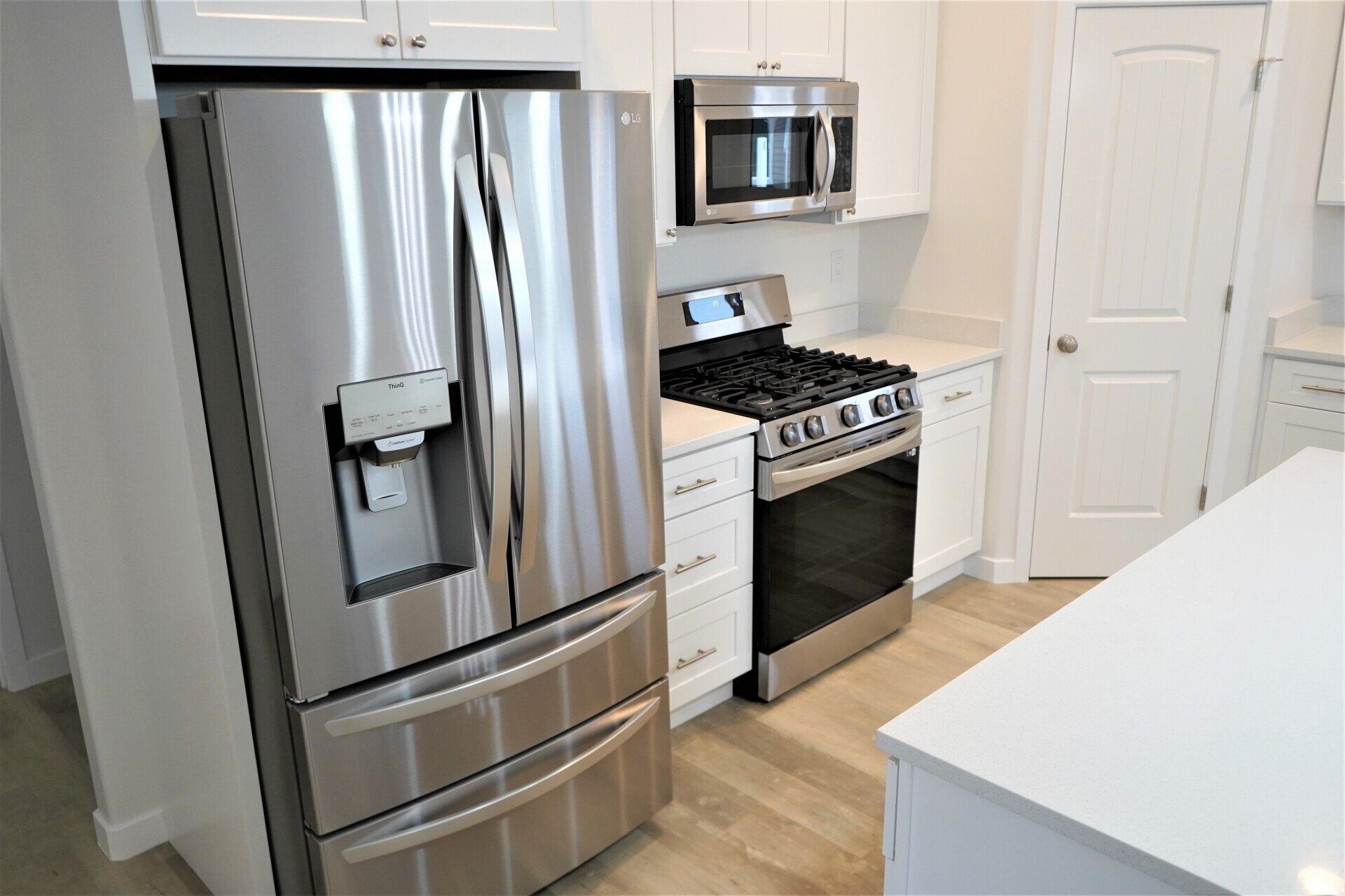 A modern kitchen with stainless steel refrigerator, gas stove, microwave, white cabinets, and light wood flooring.