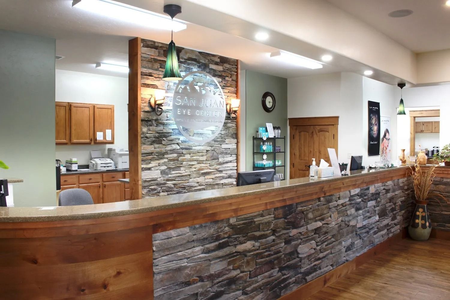 Reception desk at an eye care office with stone accents, wood cabinetry, and a circular sign on a stacked-stone wall.