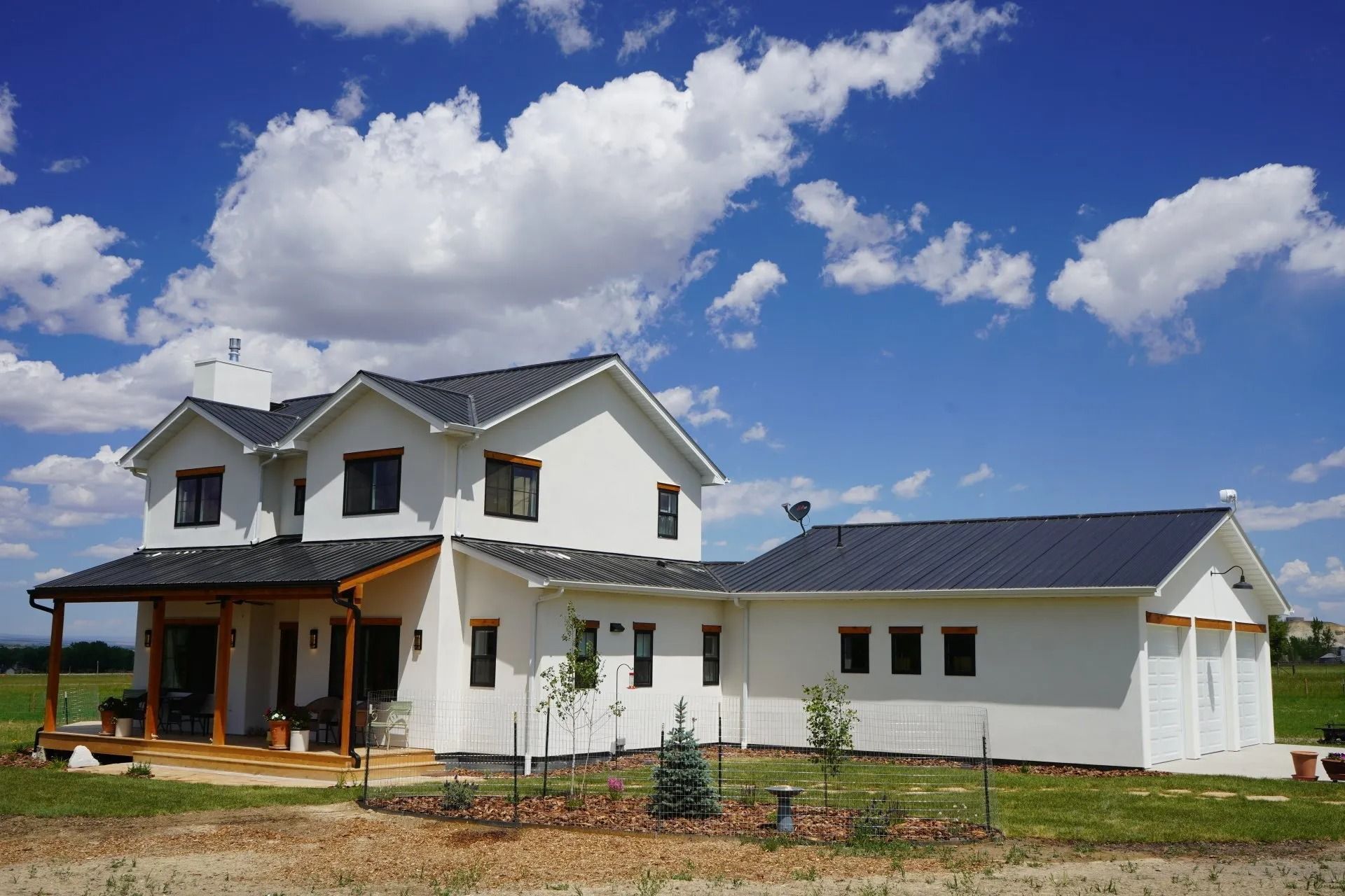 A two-story white house with a dark roof, attached garage, and front porch under a blue sky with scattered clouds.