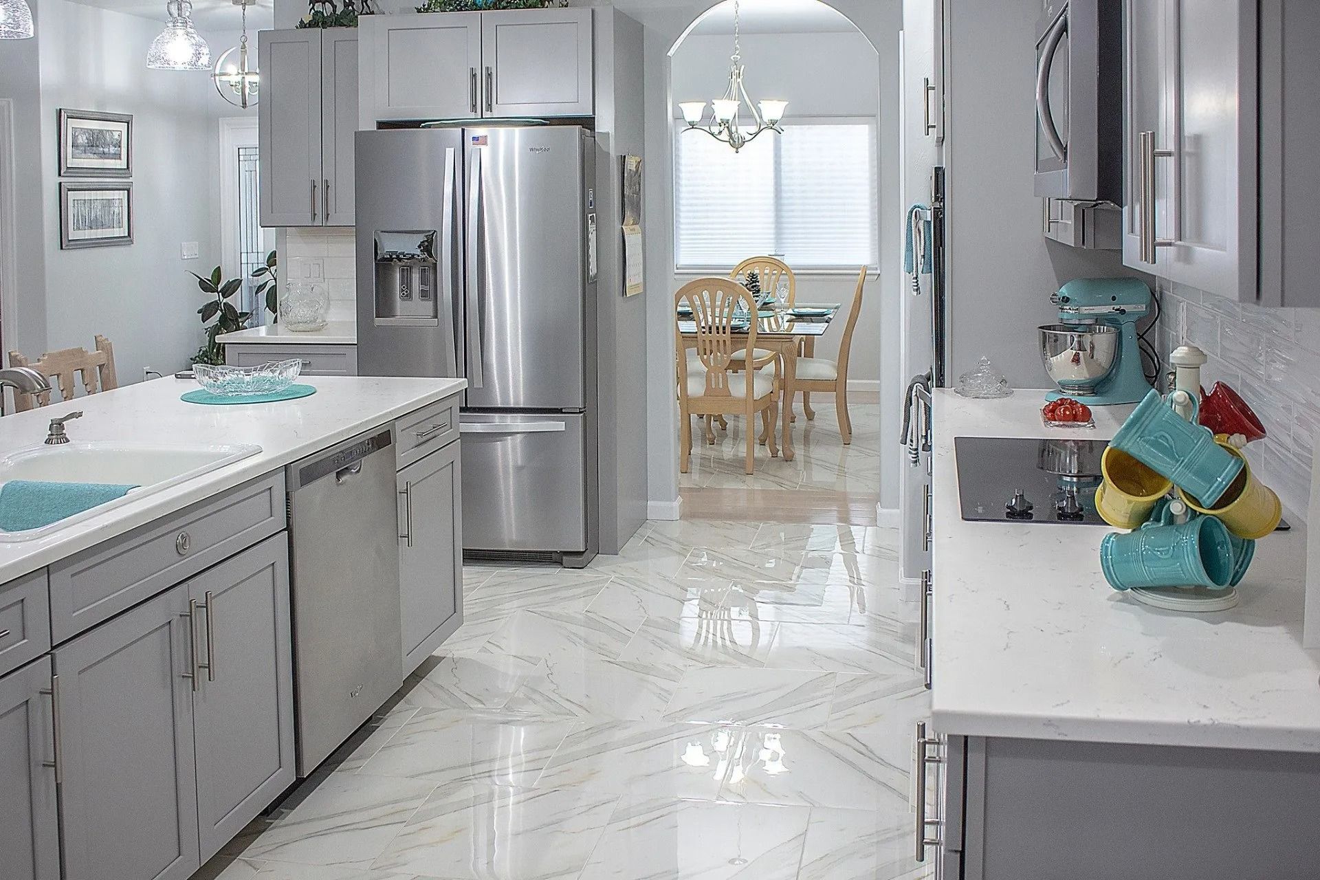 A bright, modern kitchen with gray cabinetry, white marble countertops, and light-colored tile floors.