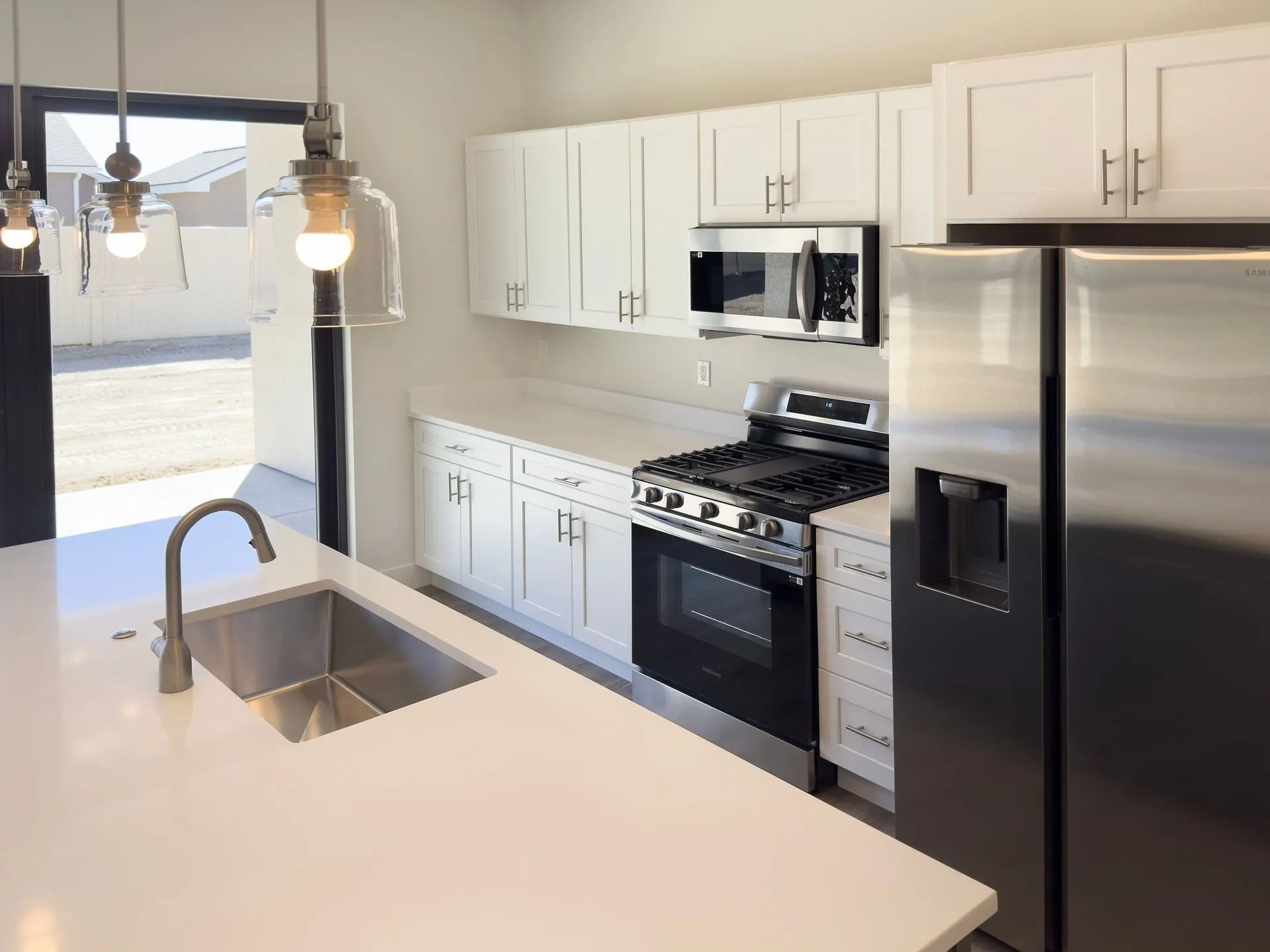 A modern kitchen featuring white cabinets, stainless steel appliances, a quartz island with a sink, and pendant lighting.