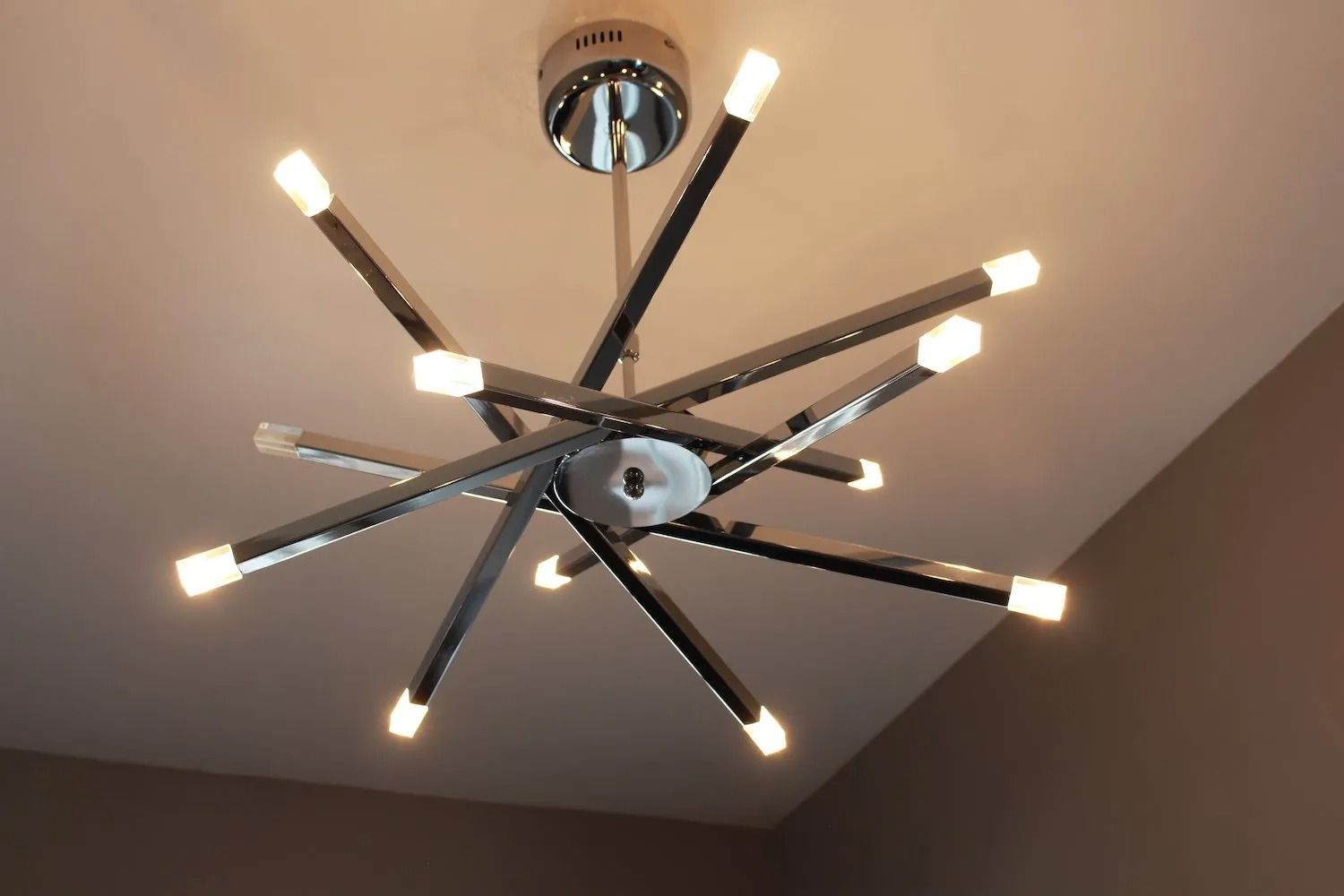 A modern chrome starburst chandelier with multiple radiating arms tipped with bright LED lights, hanging from a ceiling.