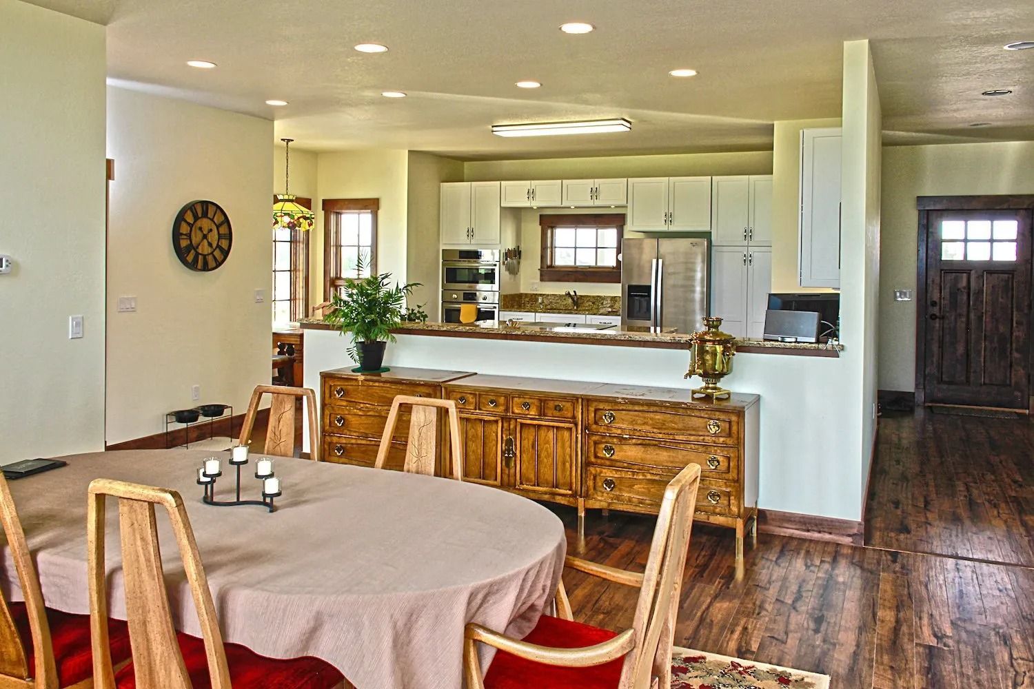 An open-concept home interior featuring a dining area with a round table, a wooden sideboard, and a kitchen in the back.