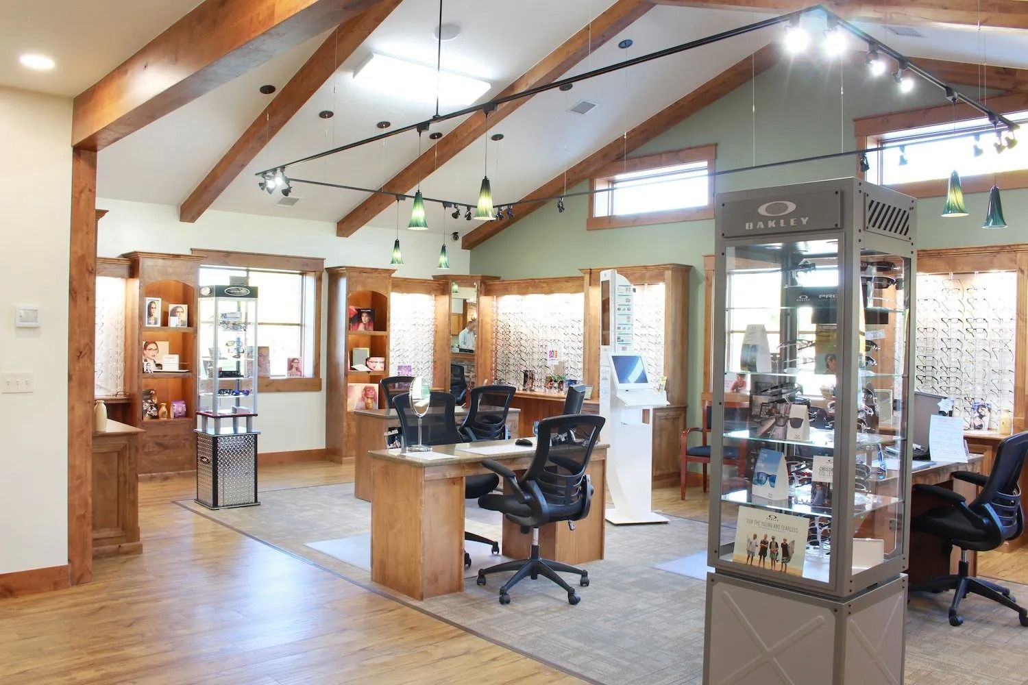 An optometry office interior featuring wooden beams, display cases, desks with chairs, and wall-mounted eyewear displays.