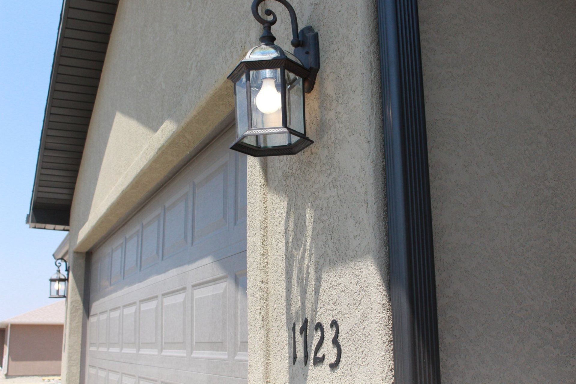 An exterior wall of a home with the address number 1123, a light fixture, and a garage door.