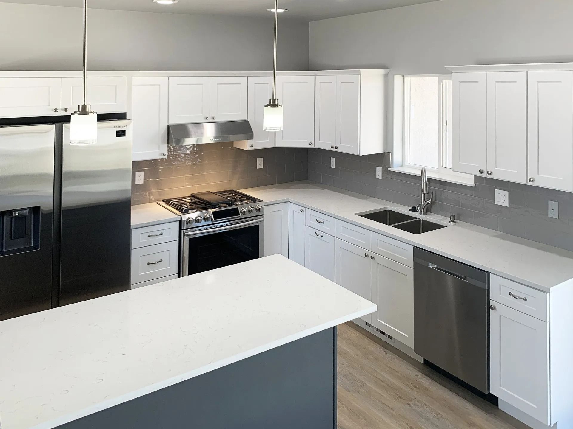 A modern kitchen with white cabinets, light countertops, stainless steel appliances, and a gray kitchen island.