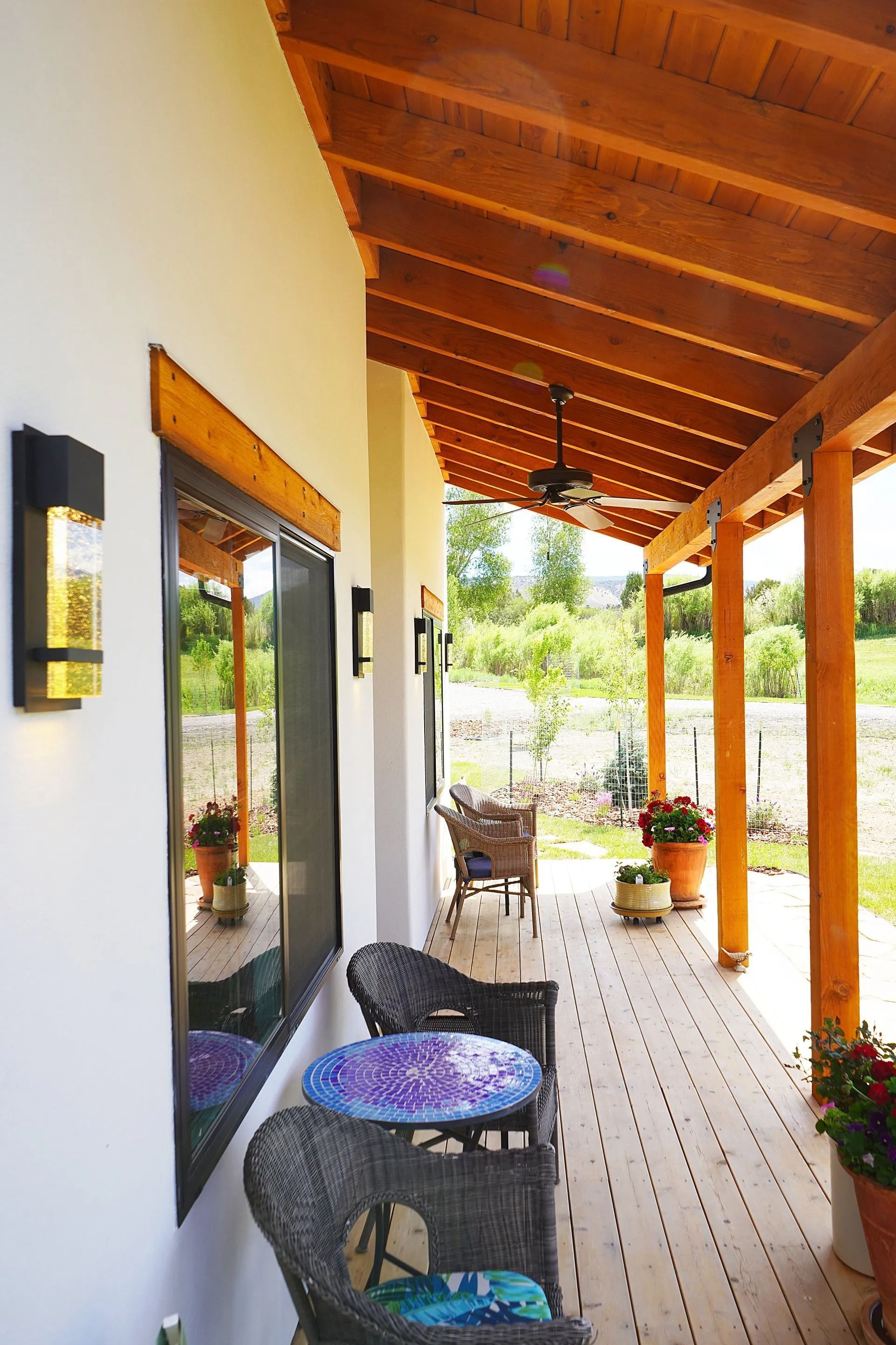 A covered porch with wooden beams, a table, and chairs, looking out onto a grassy landscape.